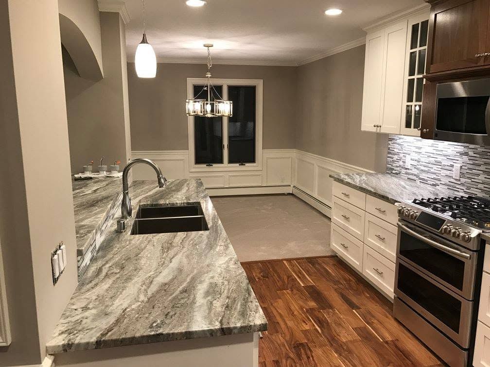 Modern kitchen with gray marble countertops, stainless appliances, white cabinets, and wood floors
