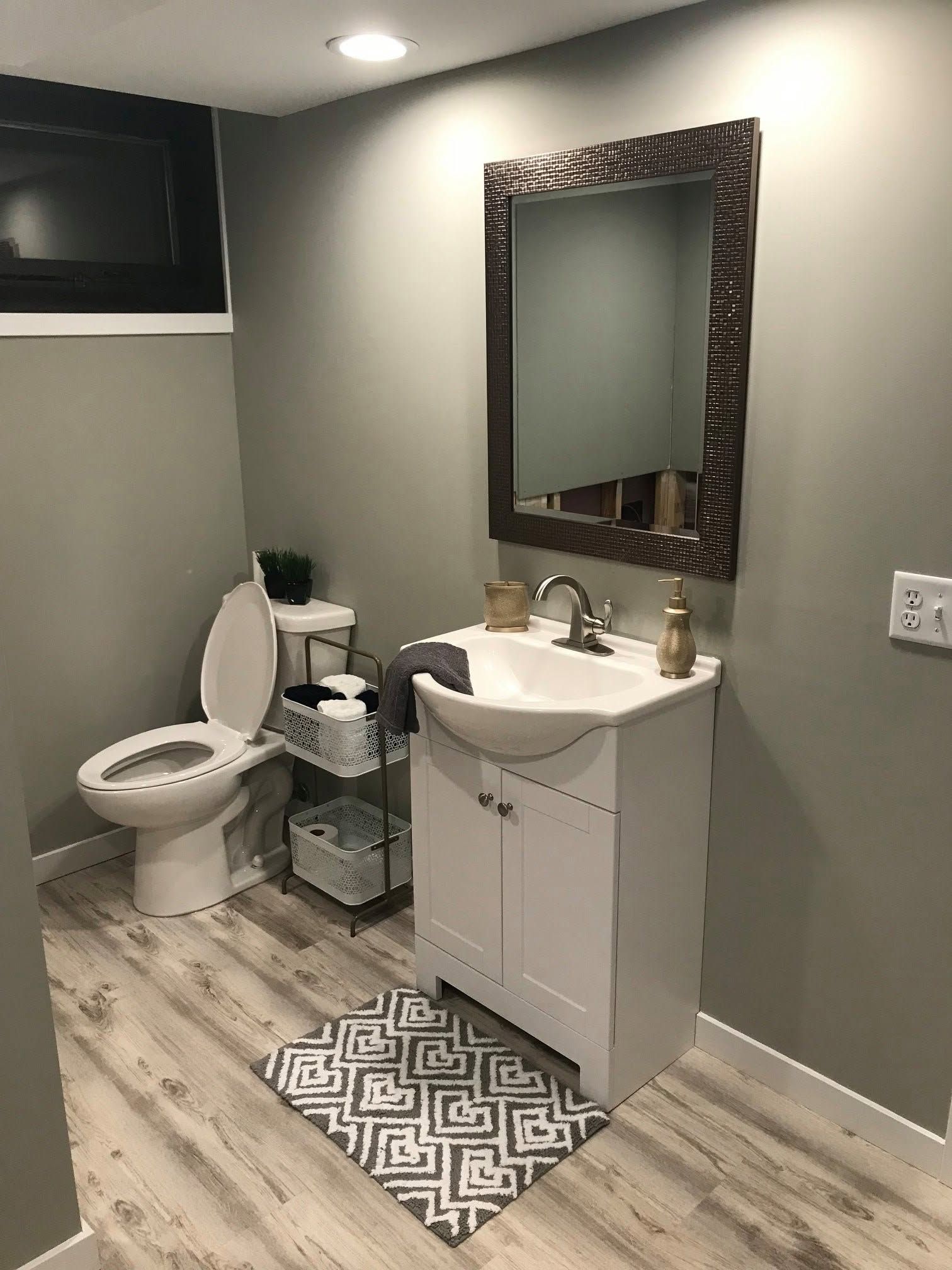 Small modern bathroom with toilet, white vanity, mirror, and gray walls.