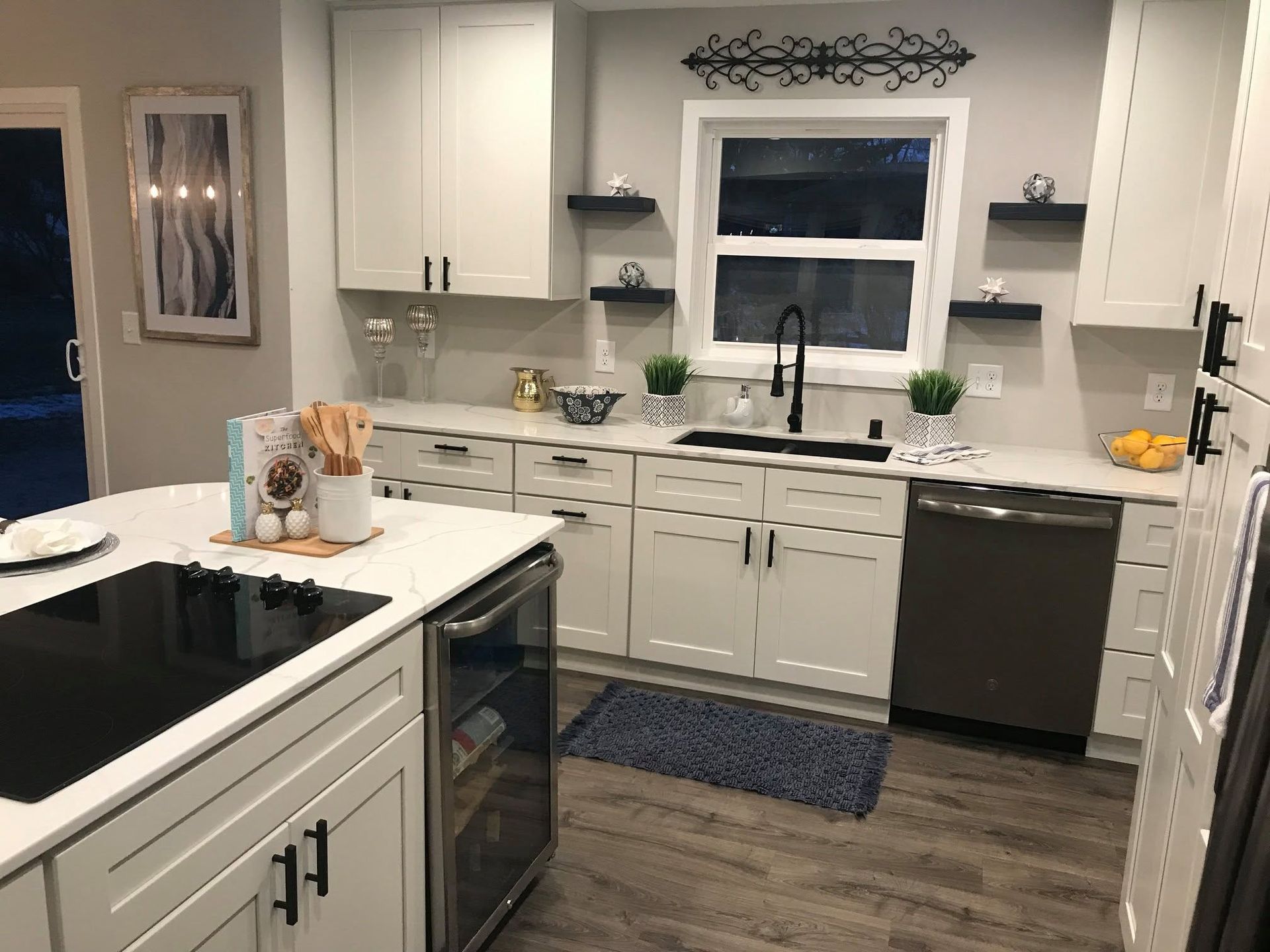 Modern white kitchen with black countertops, island, stainless dishwasher, and window over the sink