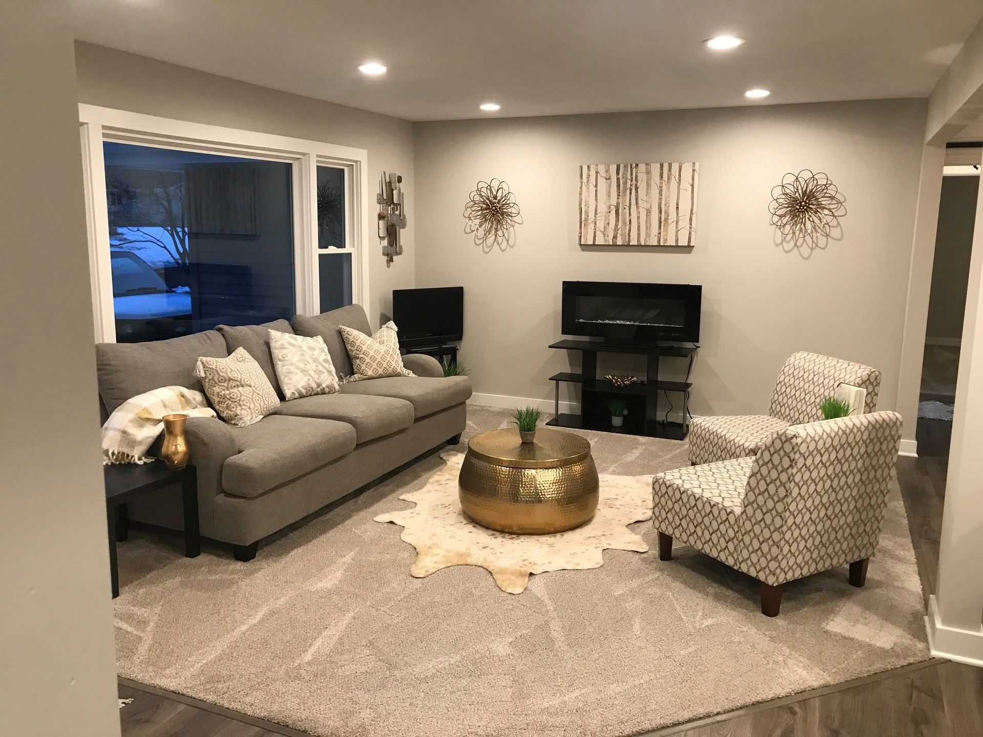 Cozy gray living room with sectional sofa, fireplace, patterned chairs, and a round coffee table