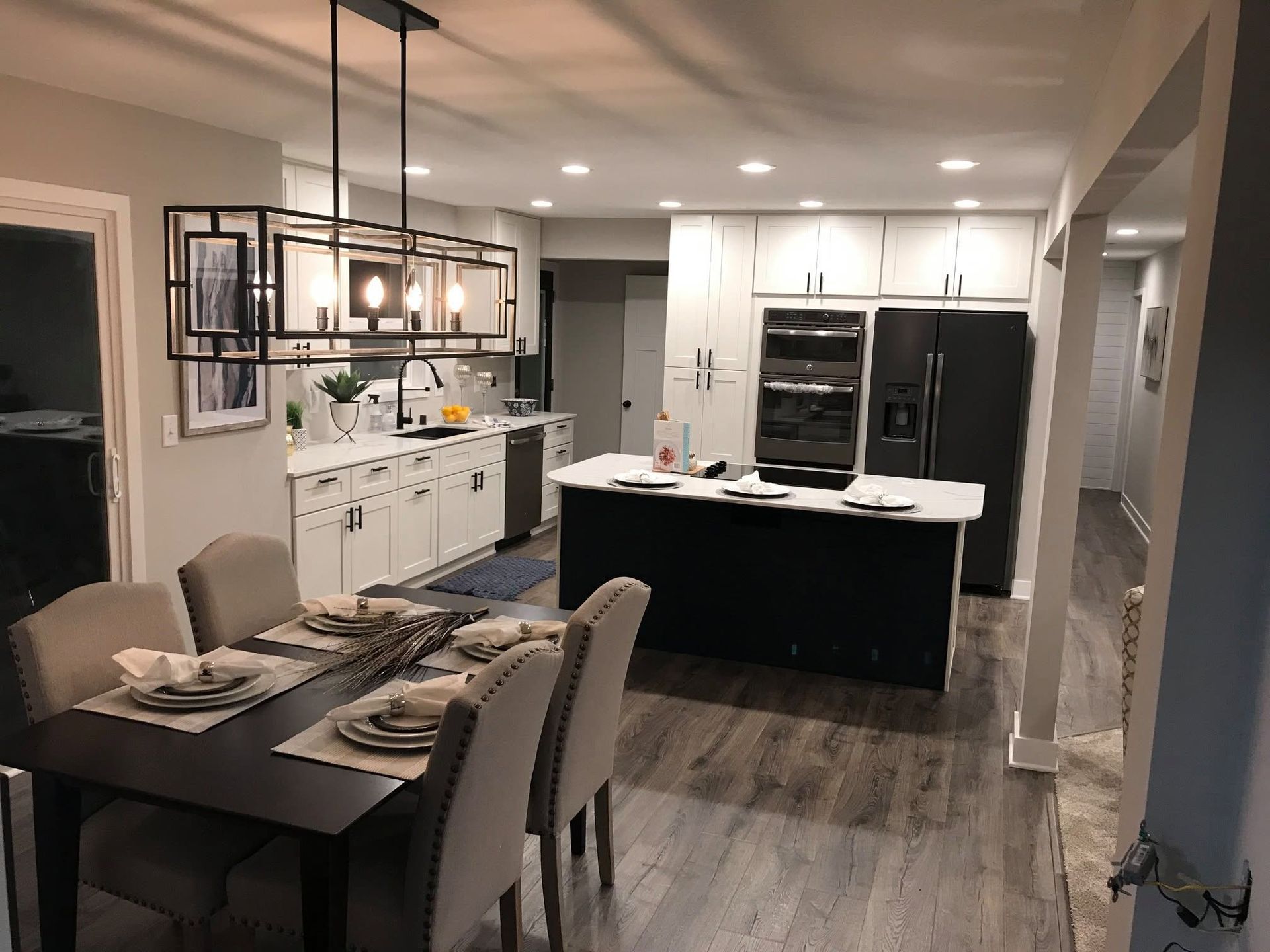 Open-concept kitchen and dining area with white cabinets, dark island, and gray chairs under pendant lights