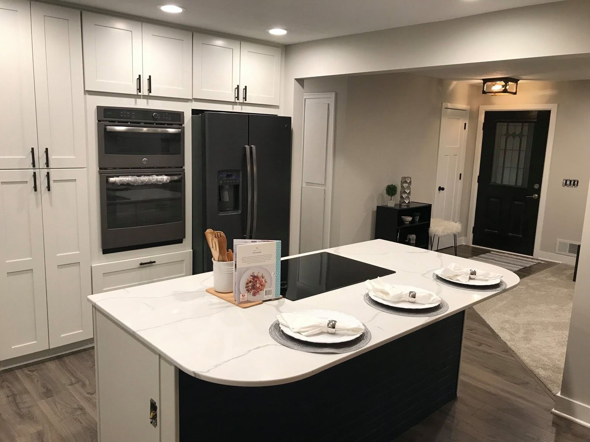 Modern white kitchen with black island, built-in ovens, and a doorway to a hallway
