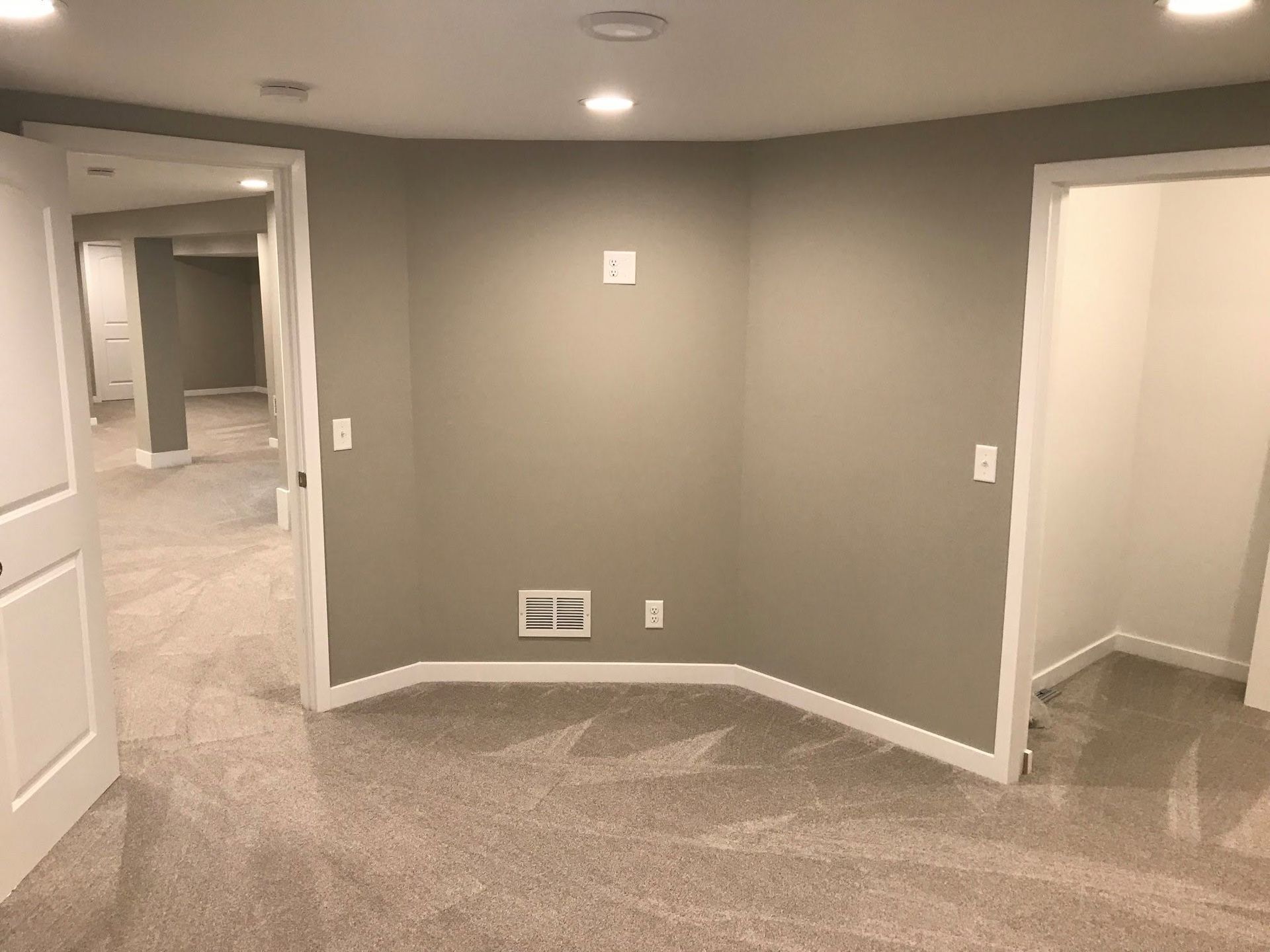 Empty carpeted room with gray walls, white trim, and open doorways leading to a hallway and closet.