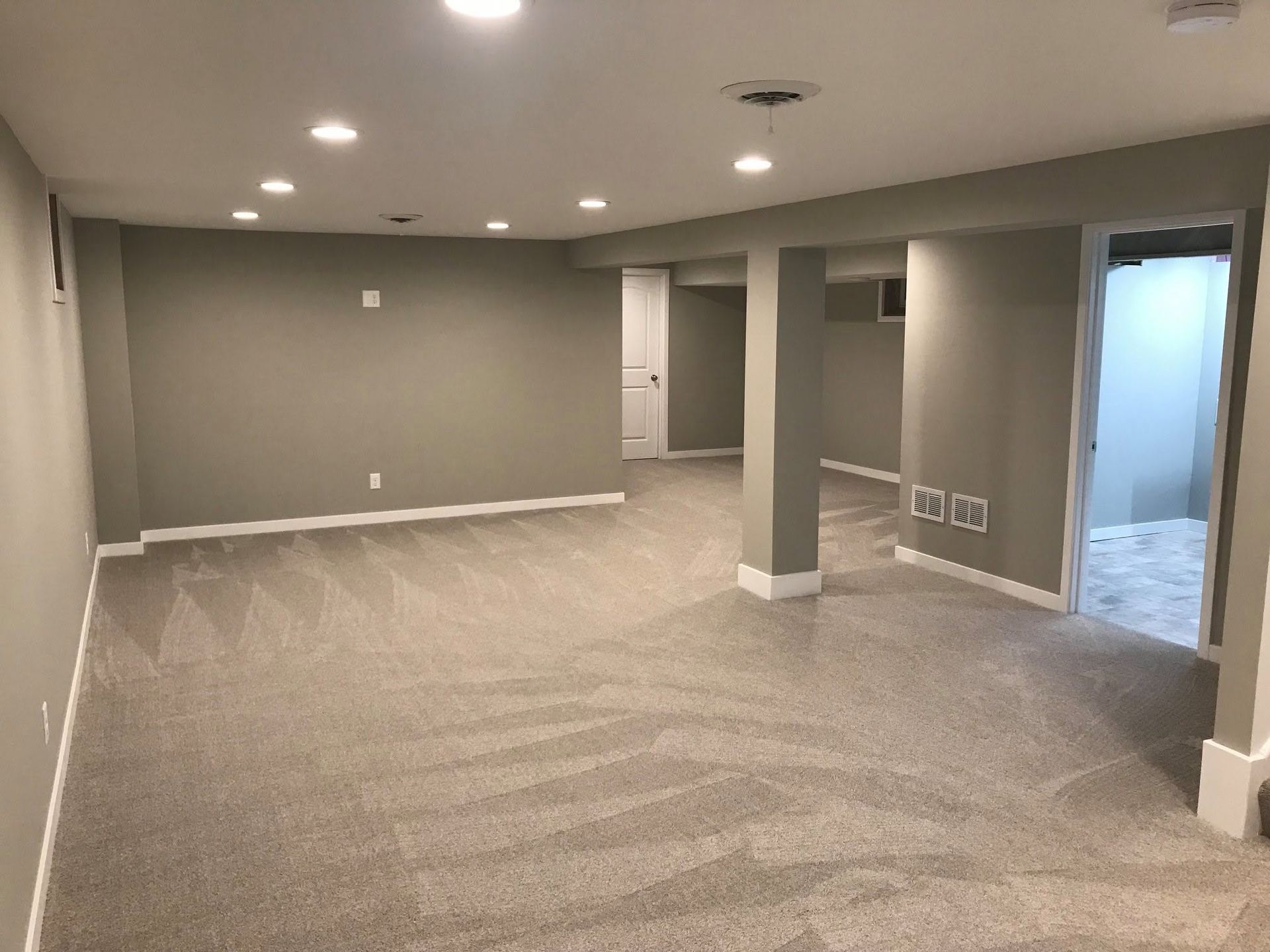 Empty gray finished basement with carpet, recessed lights, and open doorways to adjacent rooms