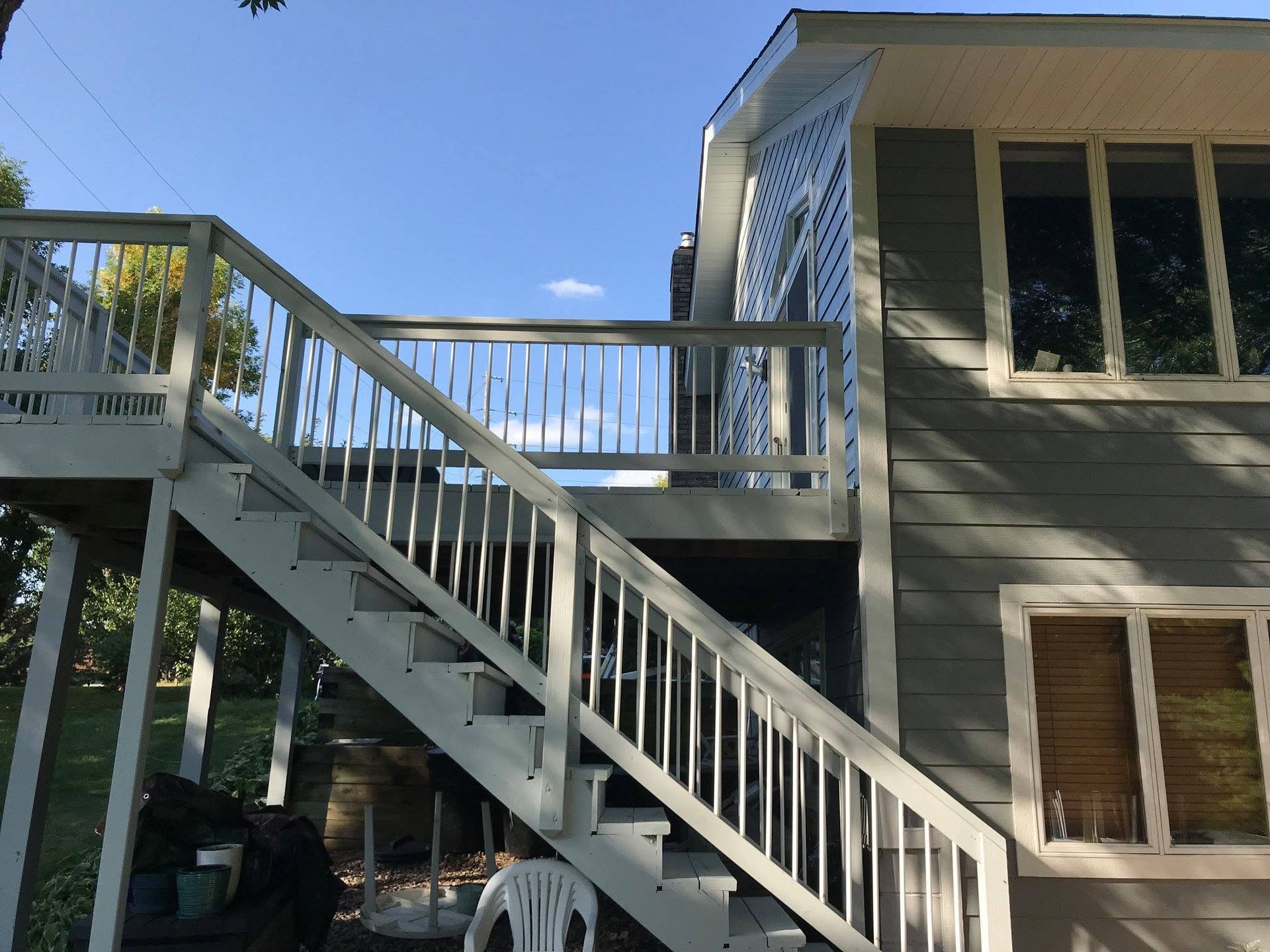 Outdoor staircase and wooden deck on the side of a gray house under a blue sky