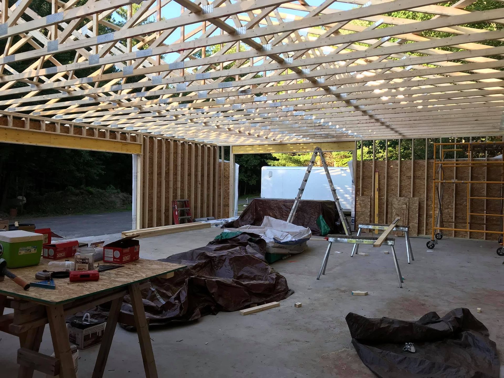 Partially built room with exposed roof trusses, wooden framing, tools, and debris on the floor.