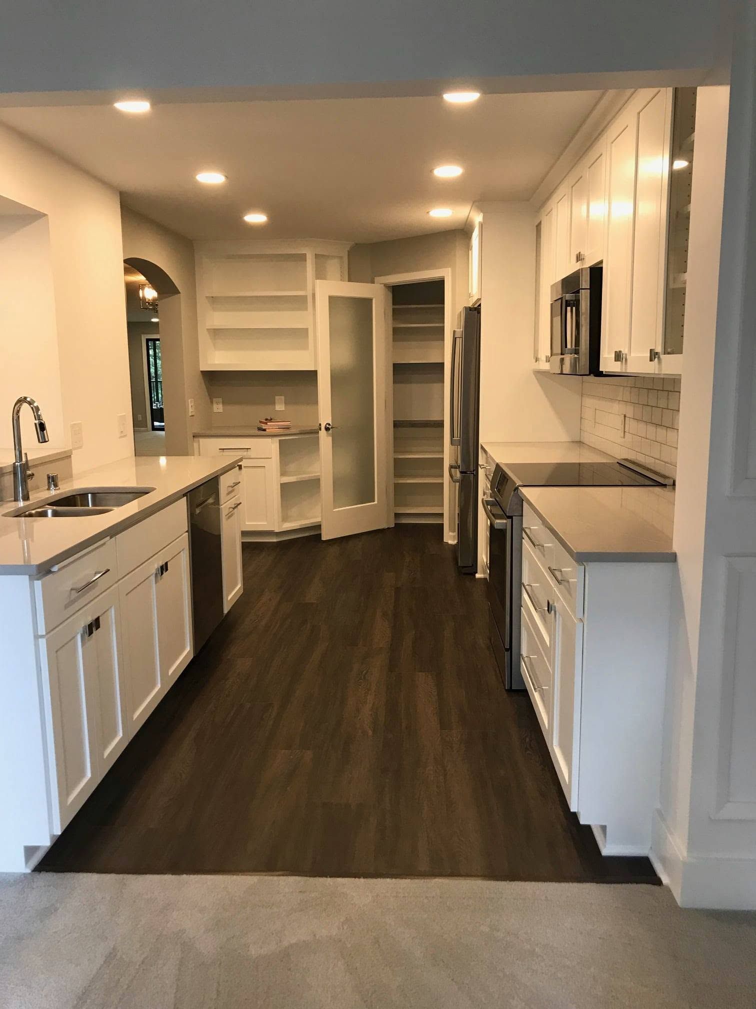 Bright kitchen with white cabinets, dark wood floor, and a narrow island under recessed lighting