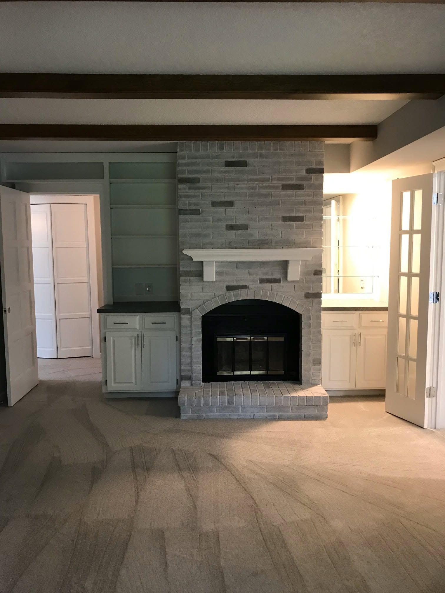 Empty room with a brick fireplace, built-in cabinets, and carpeted floor