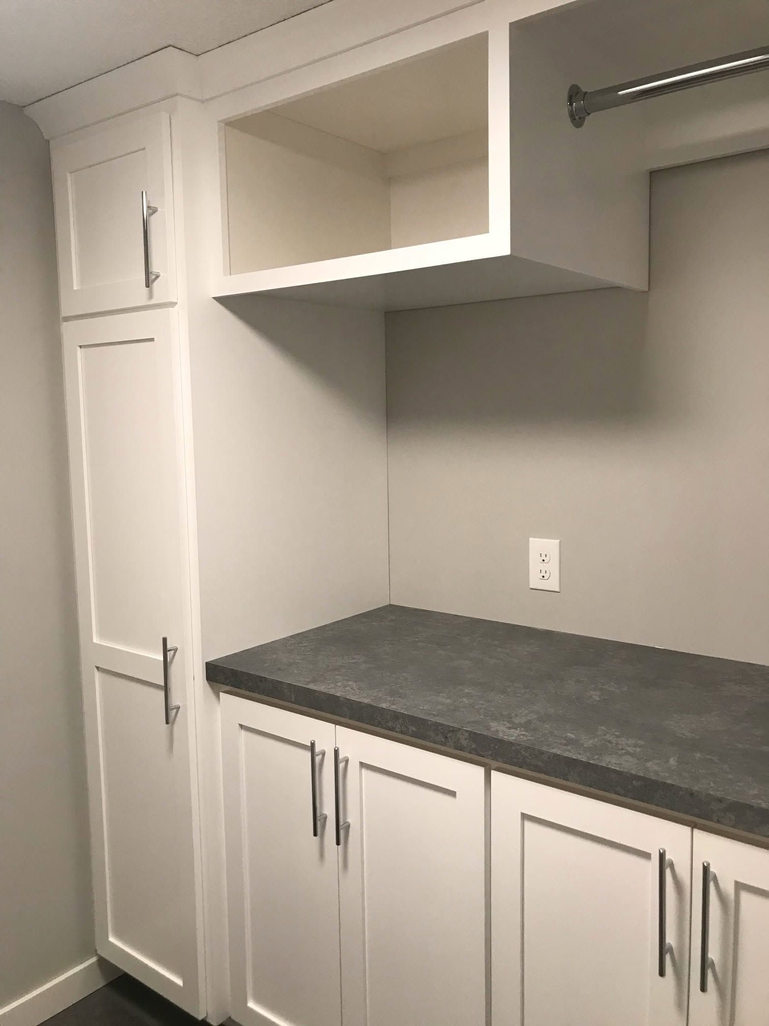White laundry room with gray countertop, cabinets, and hanging rod under a shelf.