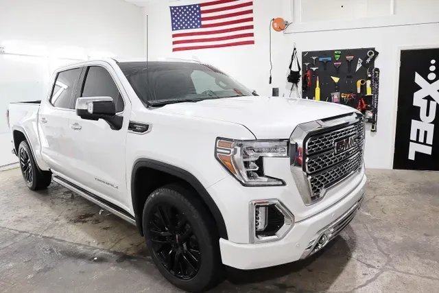 A white pickup truck is parked in a garage next to an american flag.