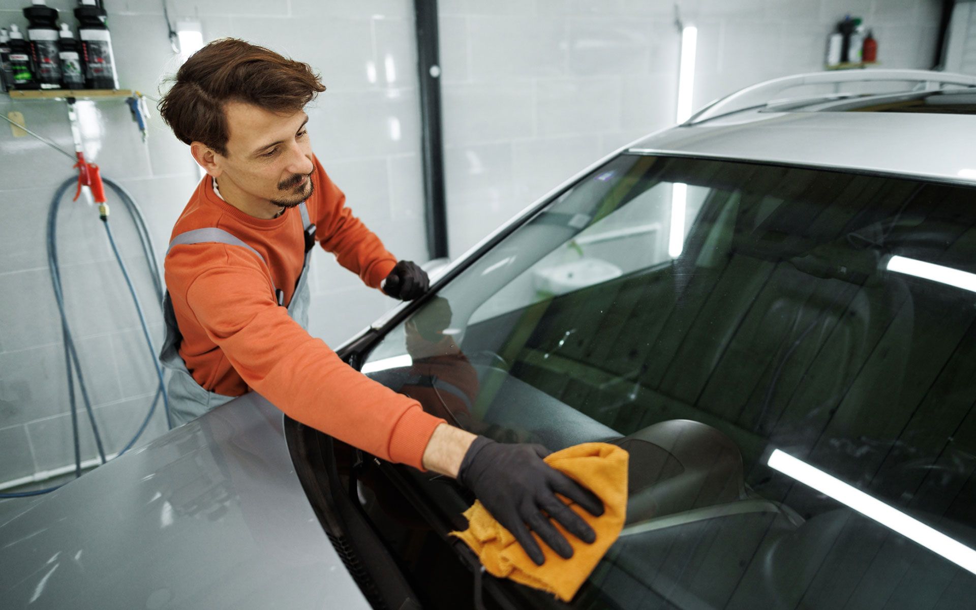 A man is cleaning the windshield of a car with a cloth.