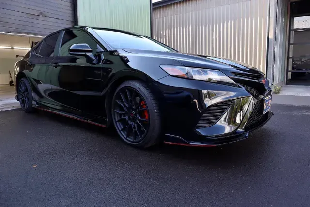 A black toyota camry is parked in front of a garage.