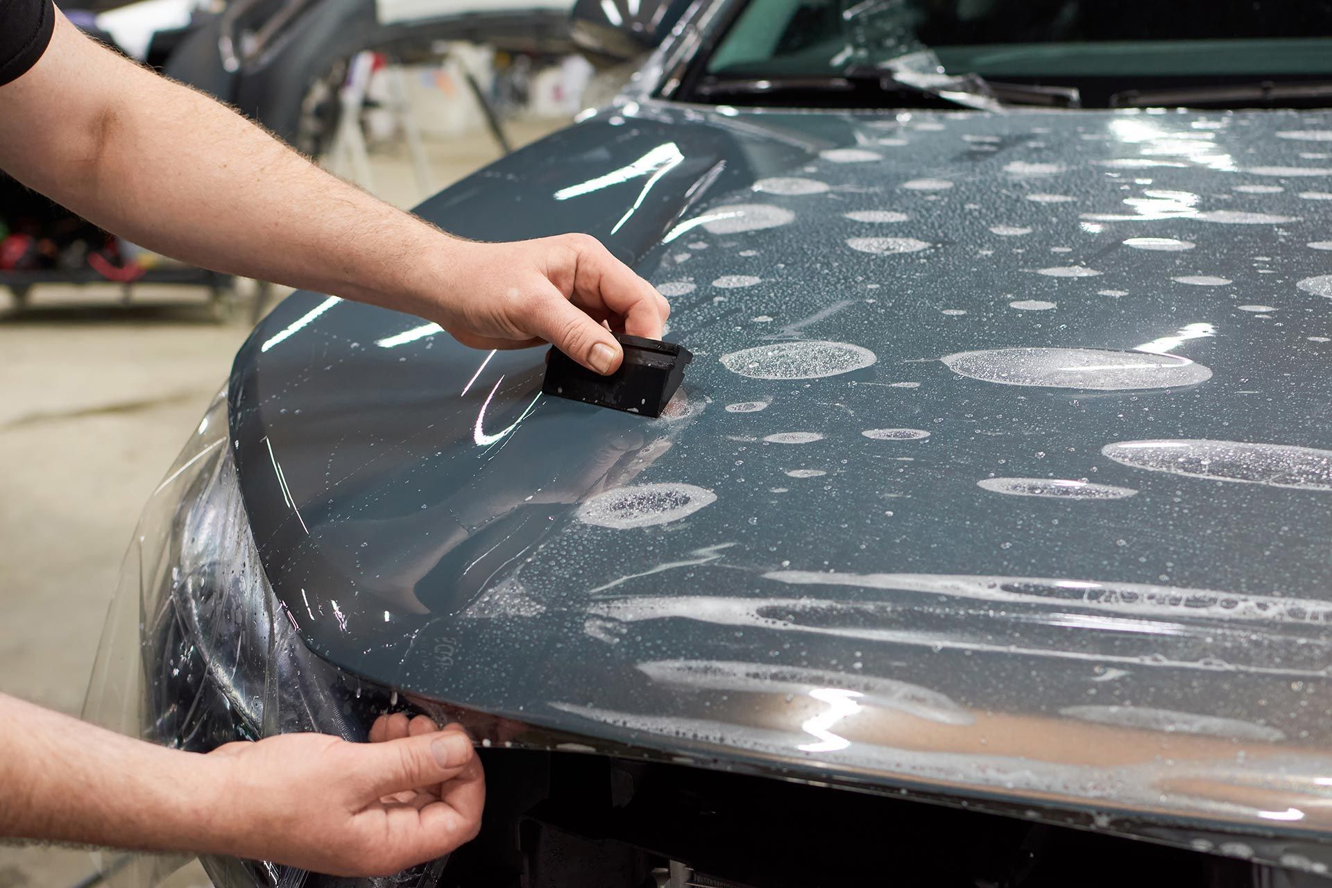 Installer squeegeeing paint protection film onto a gray car's hood Installer squeegeeing paint protection film onto a gray car's hood