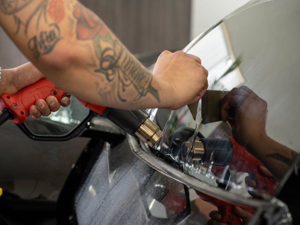 A man with a tattoo on his arm is working on a car windshield.