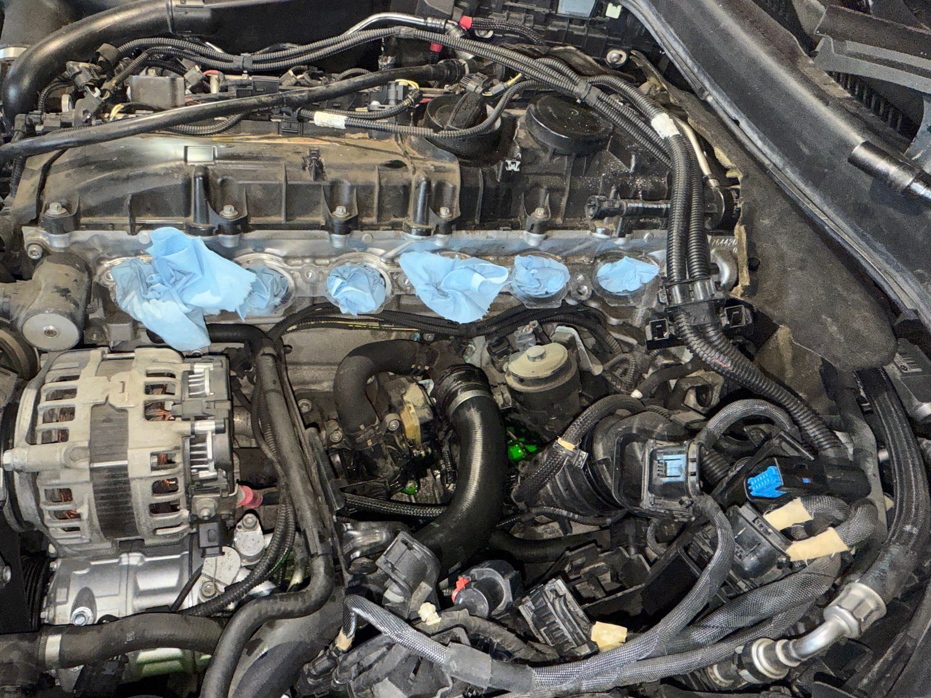 An open car engine bay with blue paper rags stuffed into the intake ports and various wires, hoses, and an alternator. | Christian's Auto Repair