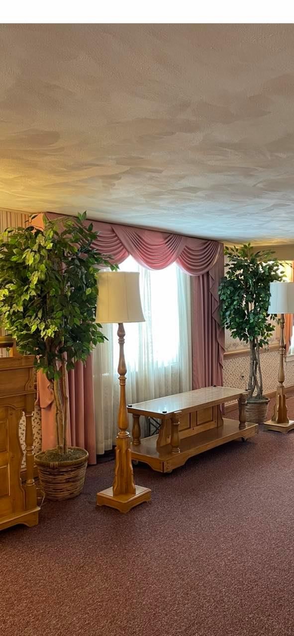 A living room with a table , lamps , trees and a window.