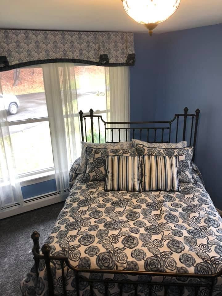 A bedroom with a bed , bench , chair and dresser. A bedroom with a bed and a window with a car parked in the background.