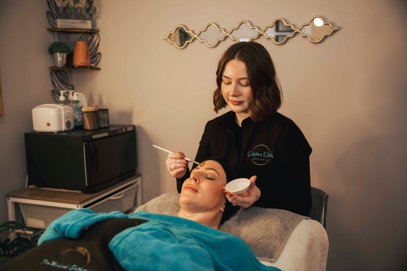 Person receiving a facial treatment while a technician applies product in a spa room