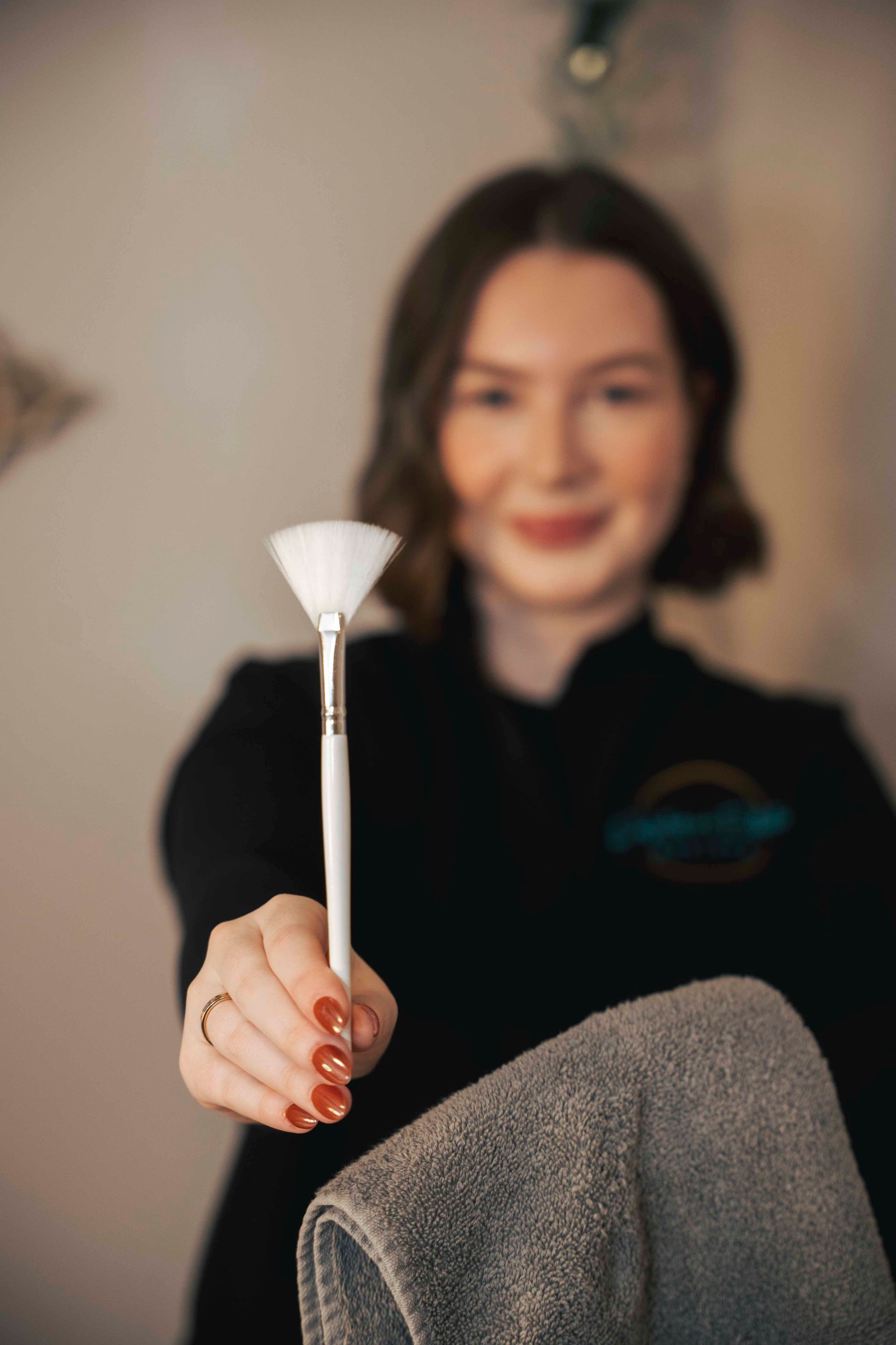Woman holding a white facial tool toward the camera, with a blurred indoor background.