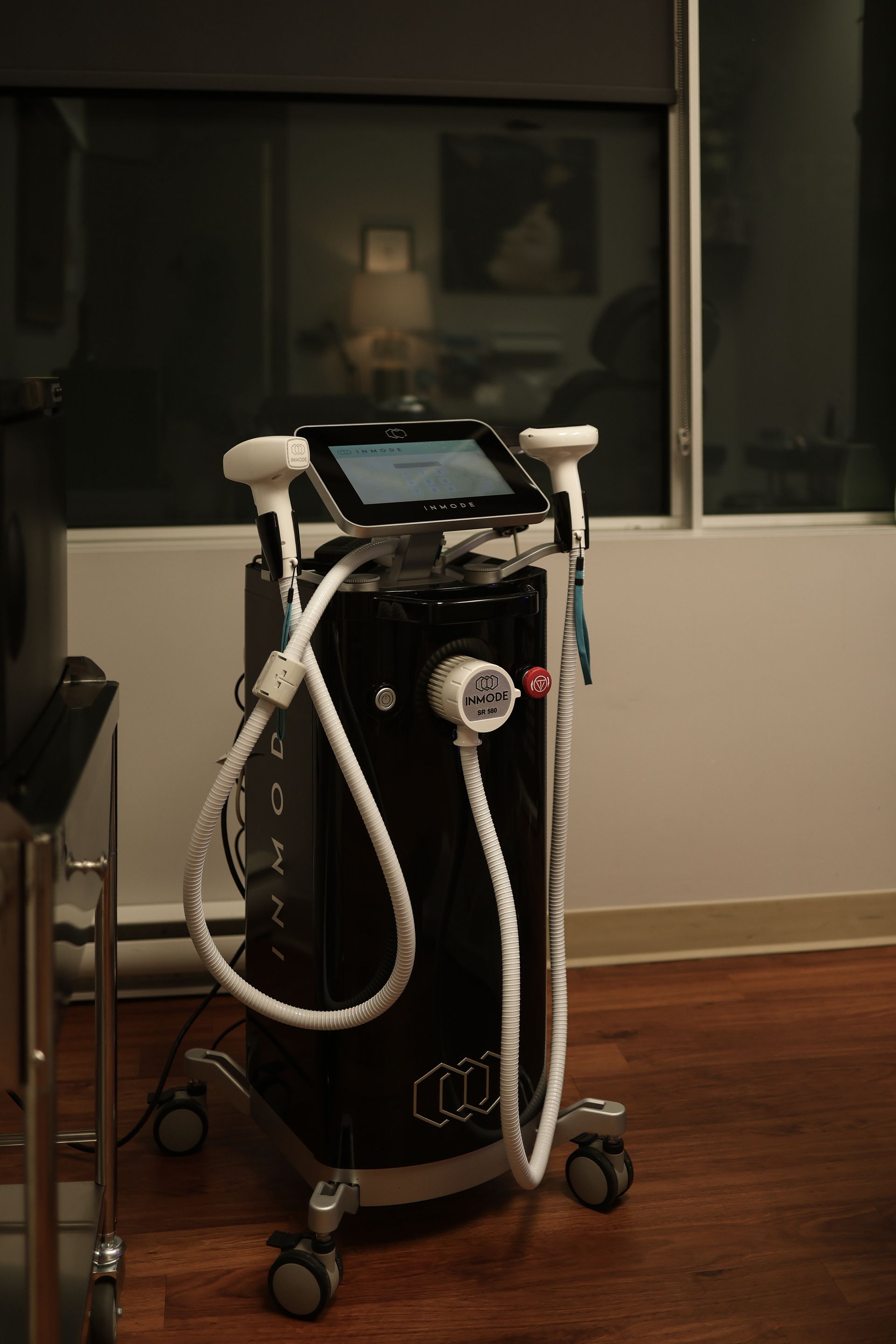 Black medical device on wheels in a room with a window, white cords attached.