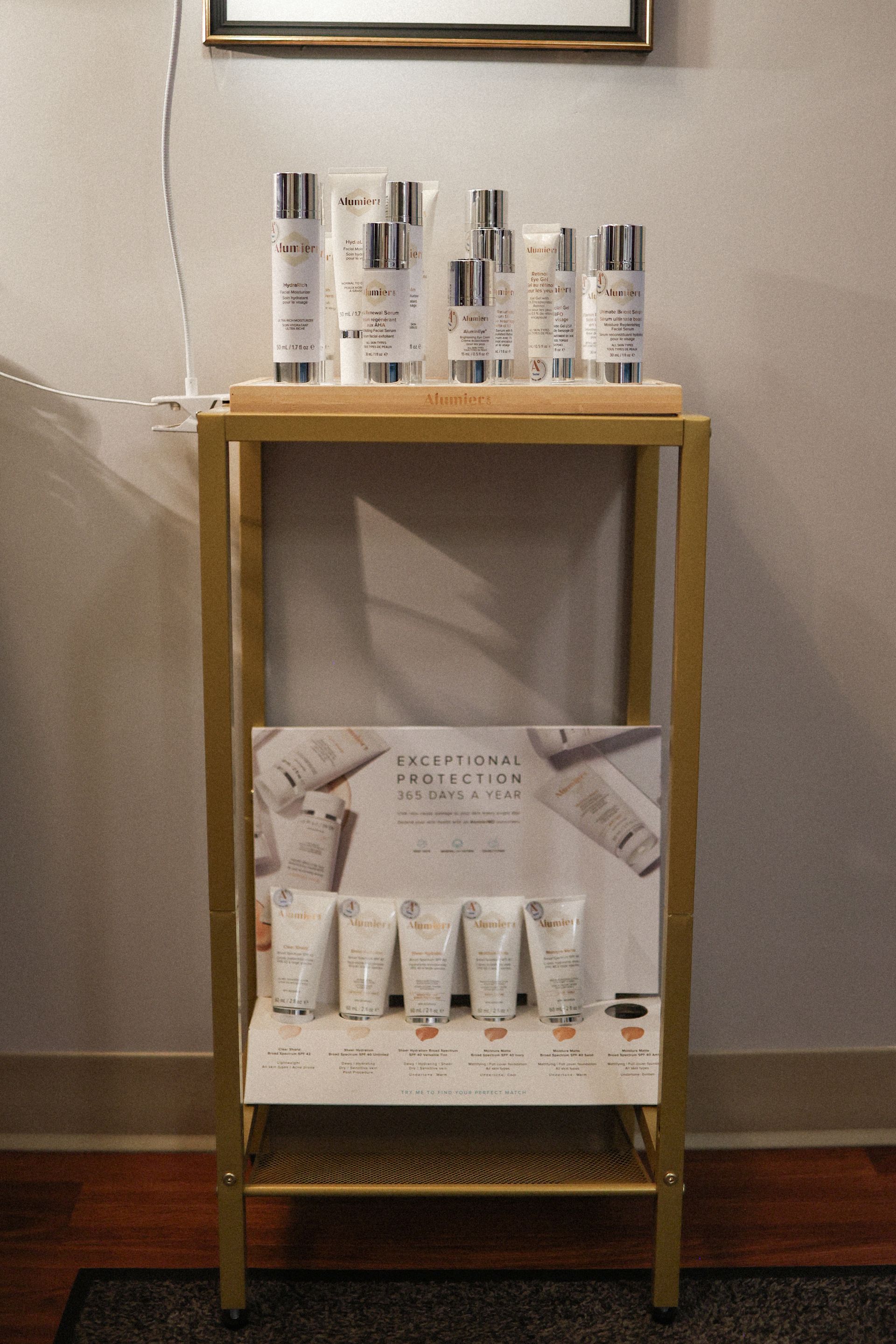 Cosmetic products on a gold shelf in a store. Several bottles and tubes are visible, with promotional signage.