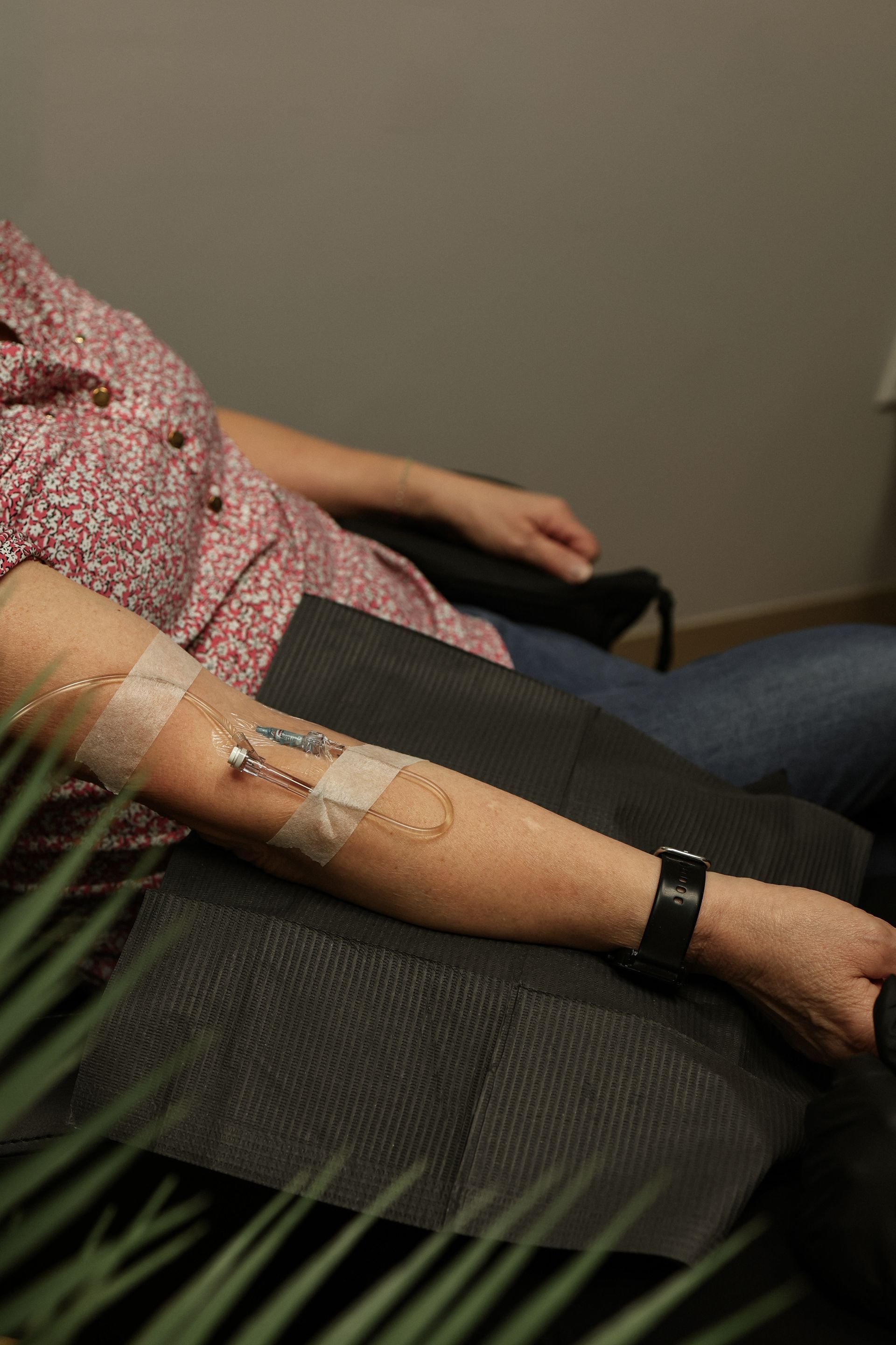Person's arm with medical equipment taped on it, likely for treatment. They are seated, possibly in a clinic setting.