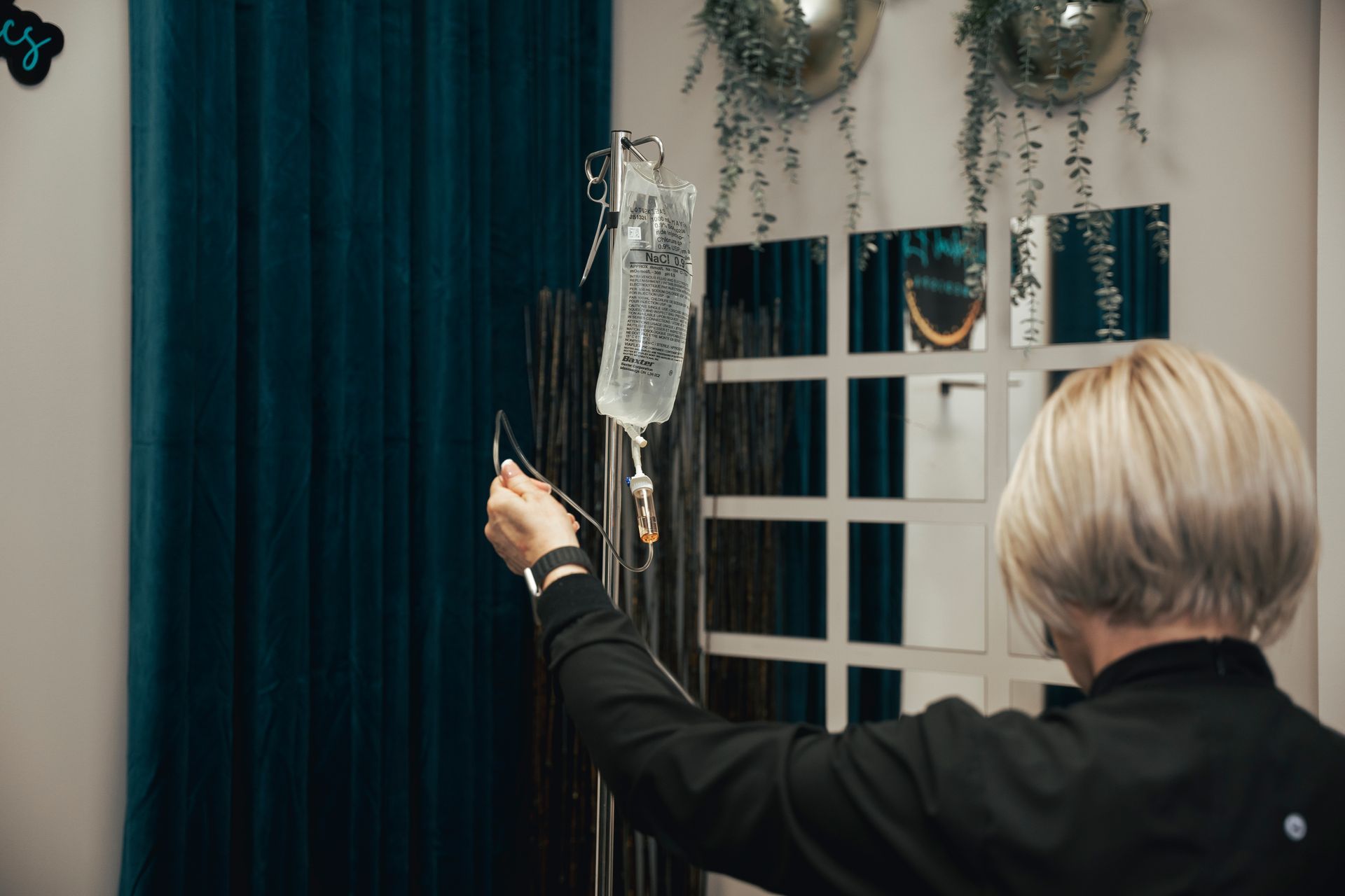 Person holding up an IV bag in a room with teal curtains and mirrors.