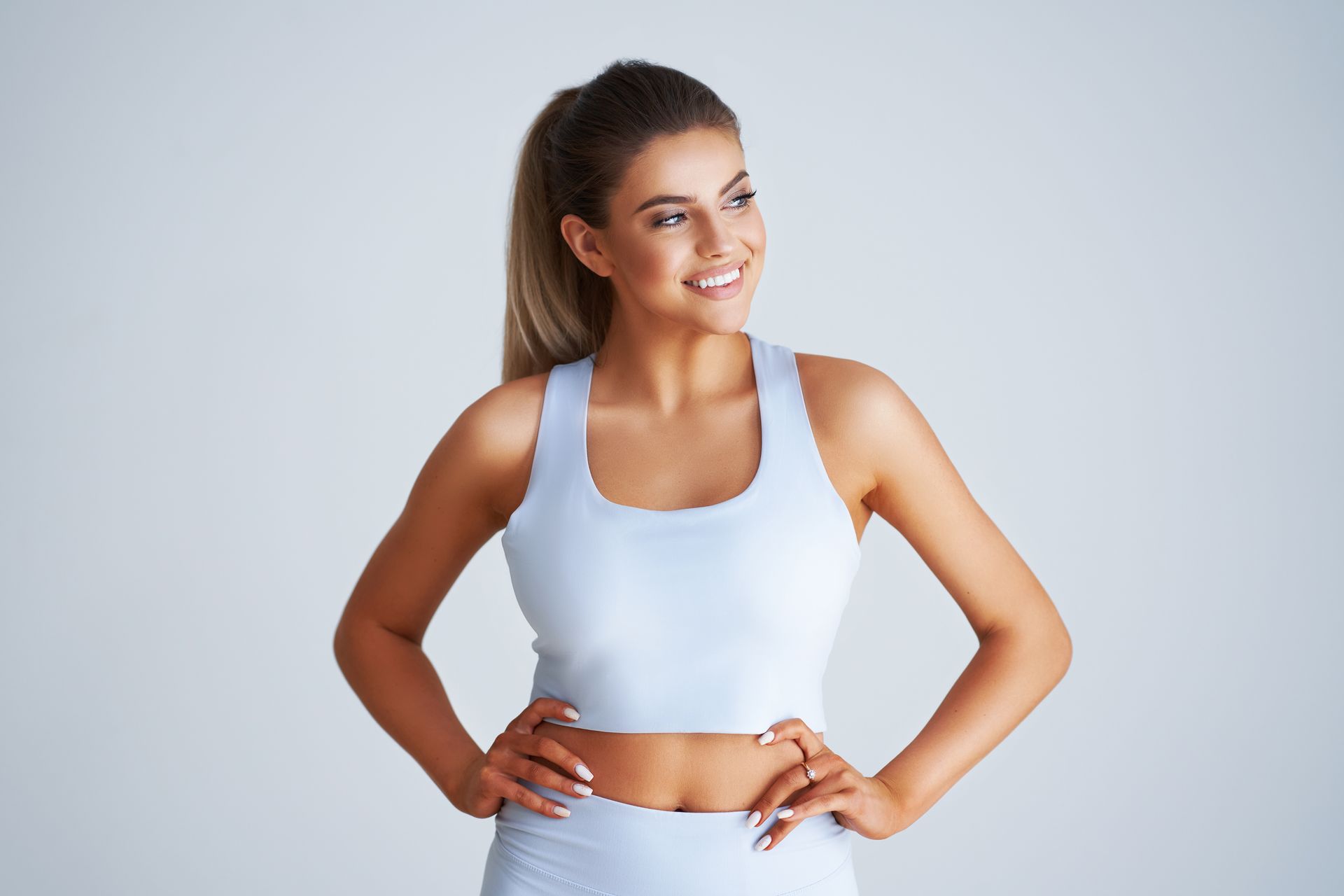 Woman in light blue athletic wear smiles, hands on hips, looking to the side.