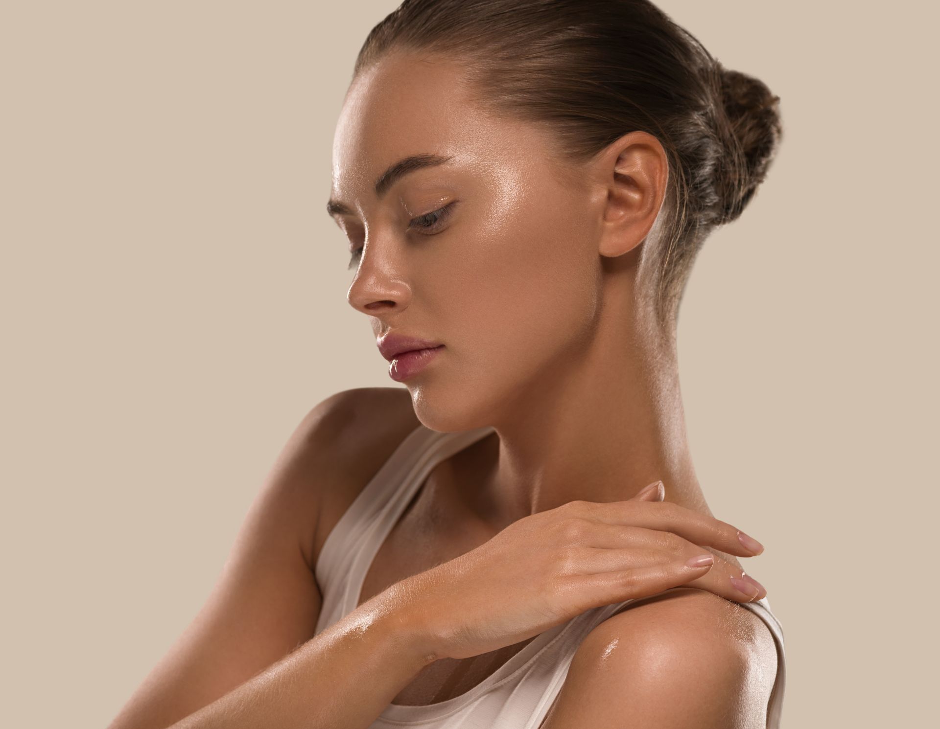 Woman with slicked-back hair and makeup, touching her shoulder, against a beige background.