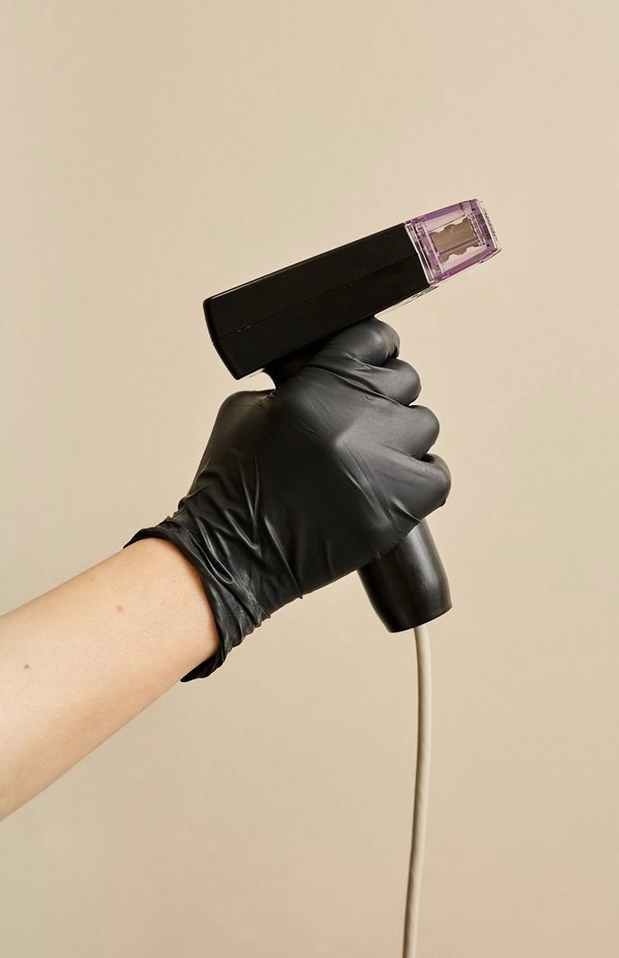 Person in black glove holding a black medical device with purple grid, white wire.