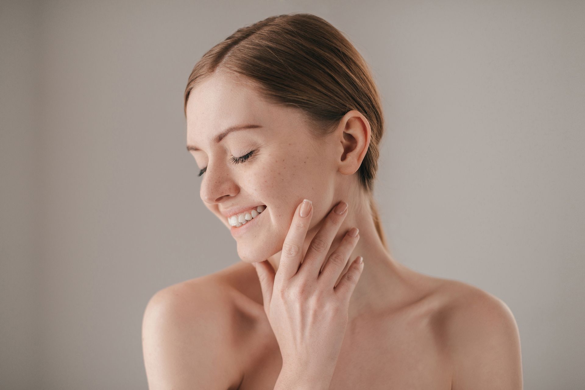 Woman with fair skin, smiling, touching her cheek.