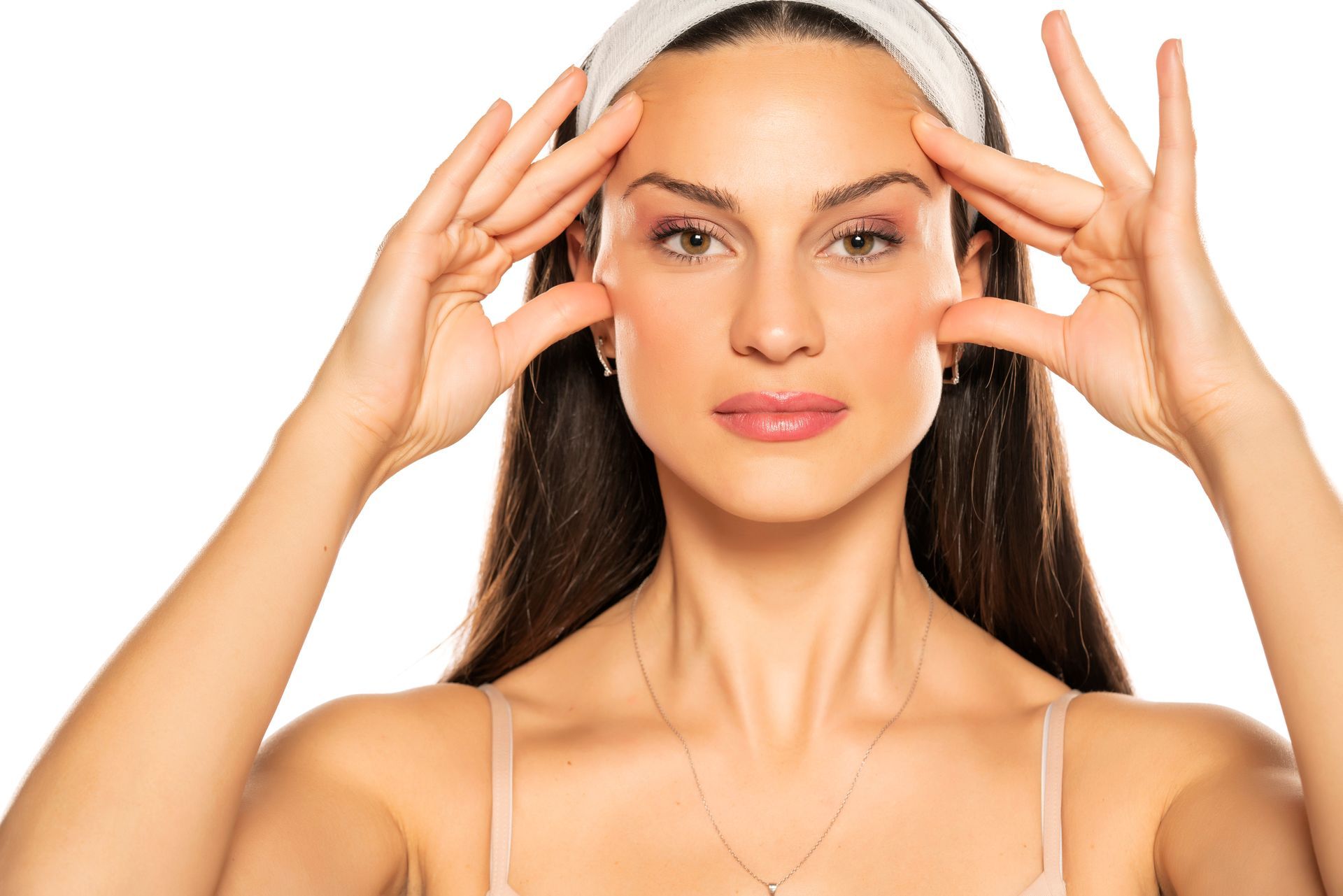 Woman with hands near her temples, wearing a white headband, against a white background.