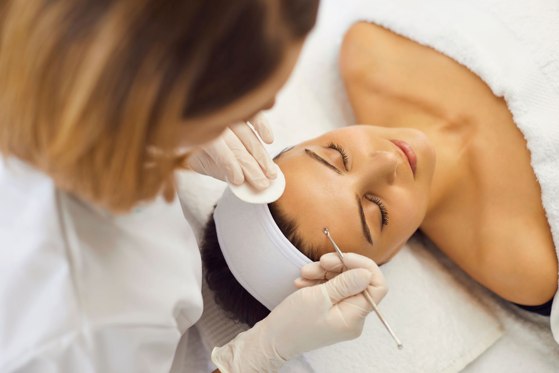 Cosmetic procedure in progress: clinician applying treatment to a client lying on a spa bed