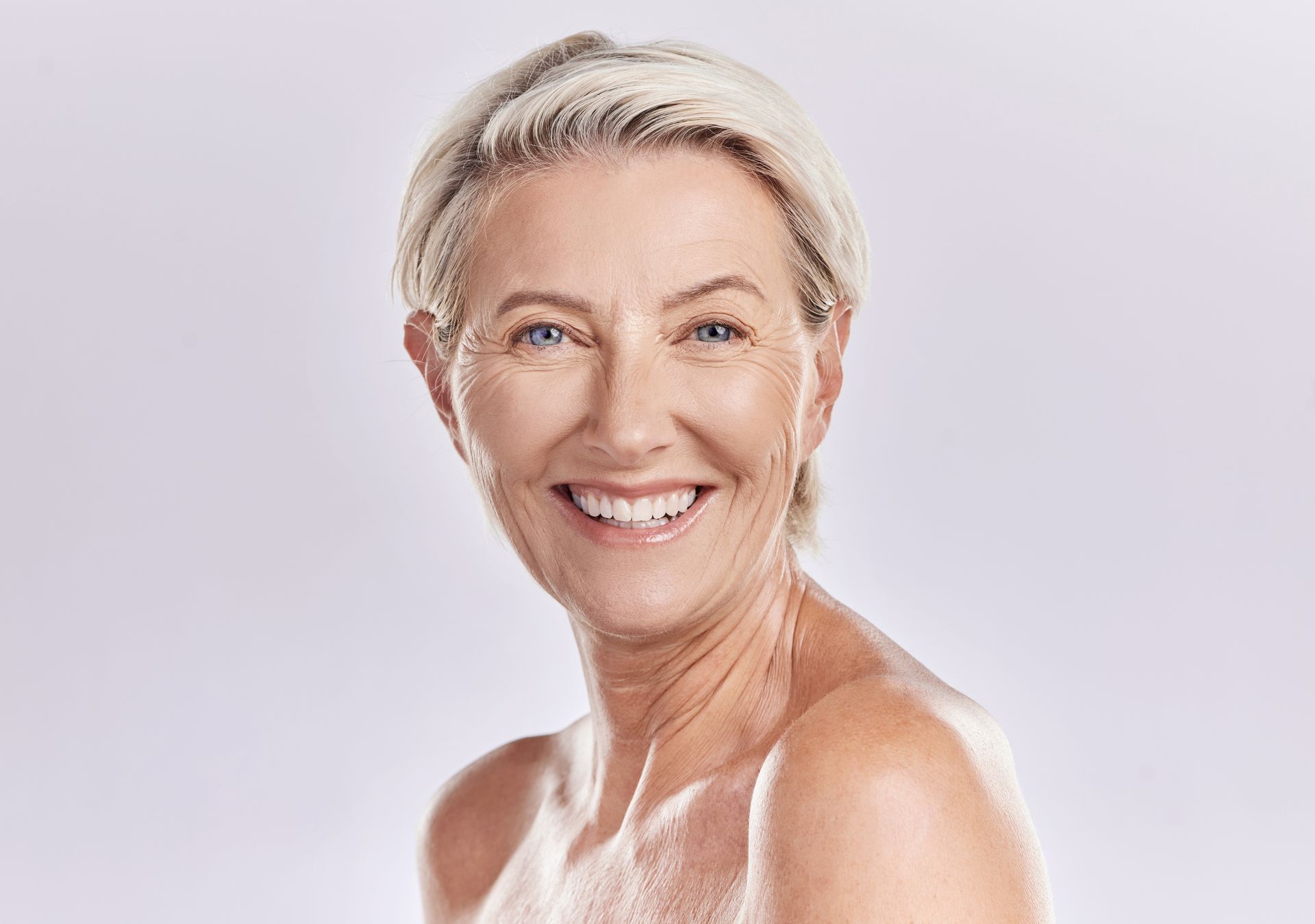 Smiling person with short white hair against a soft lavender background