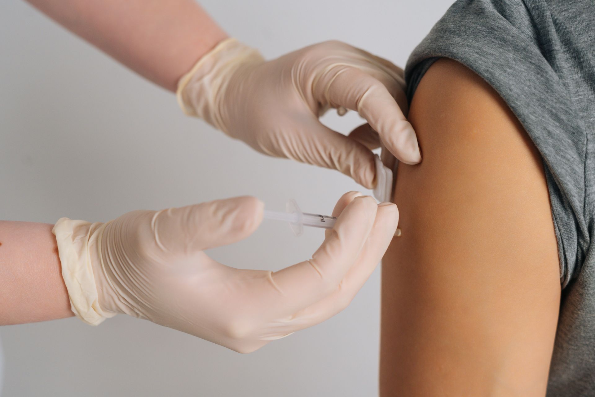 Gloved hands giving an injection to a person’s upper arm
