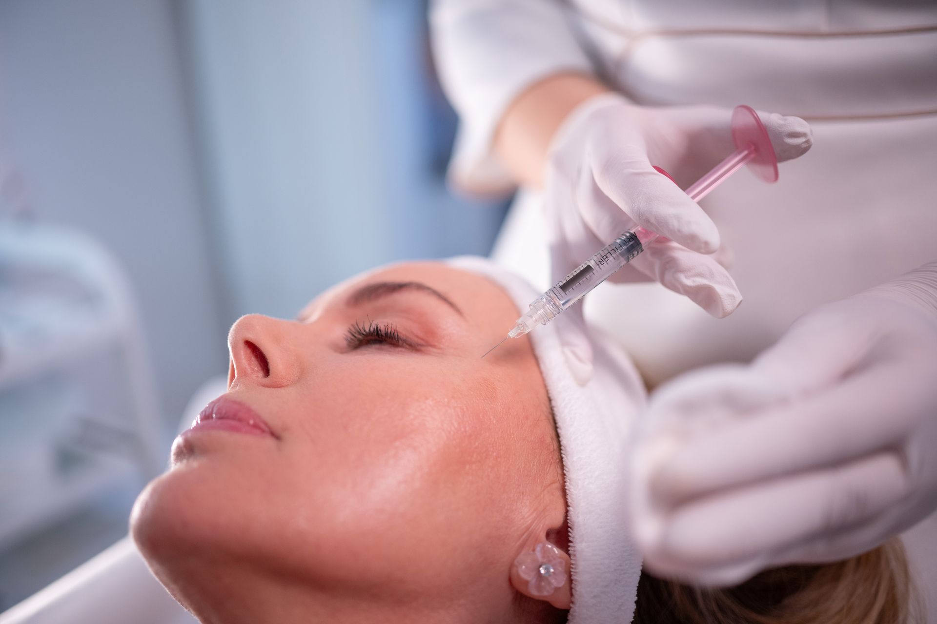 Cosmetic injector administering facial treatment with a syringe to a reclining client