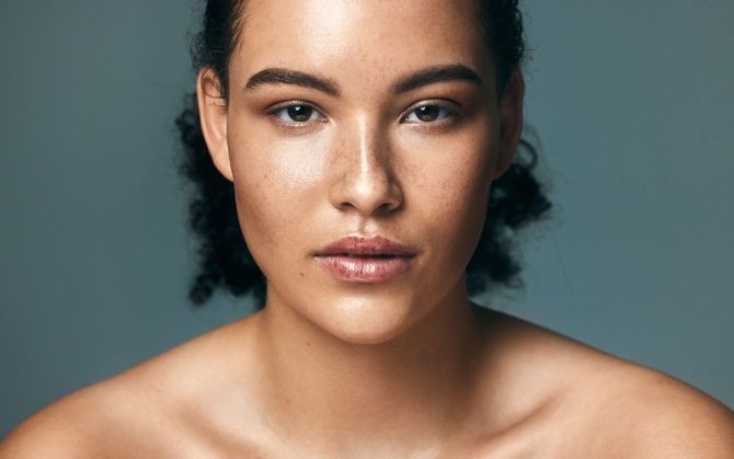 Portrait of a person with bare shoulders against a gray background, looking directly at the camera