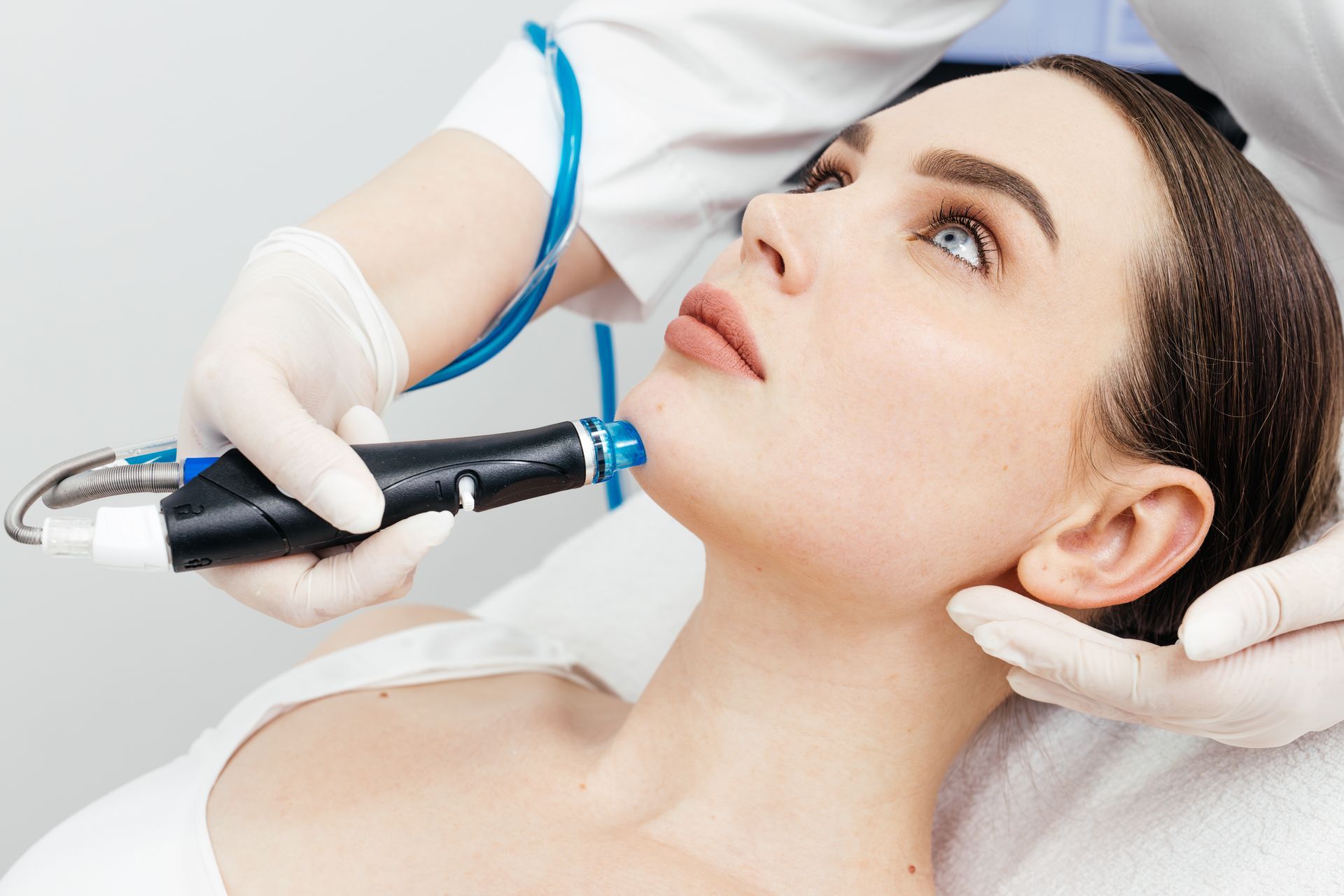 Cosmetician using a facial device on a reclining client in a bright spa setting