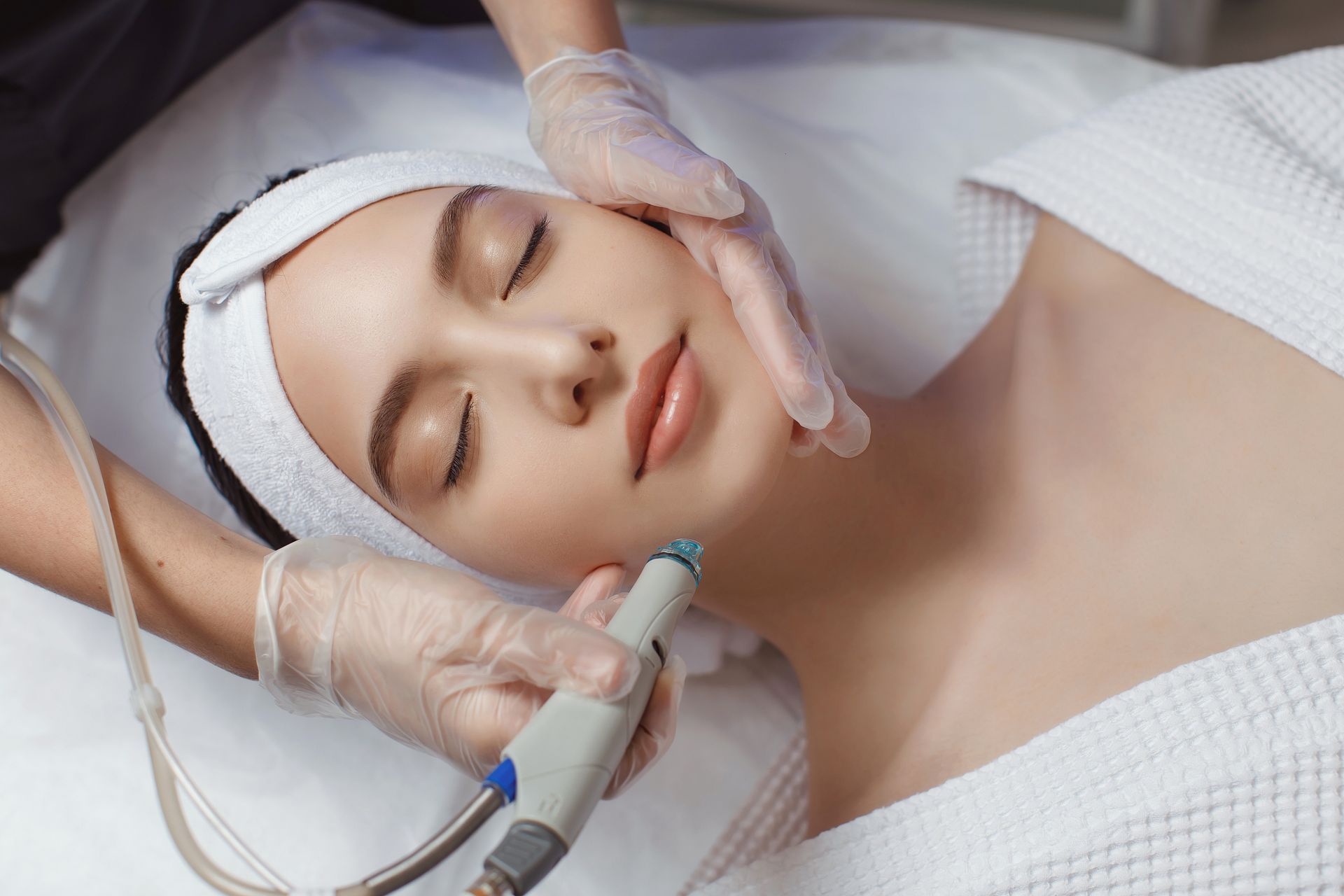Woman receiving facial treatment at a spa; hands in gloves, close up.
