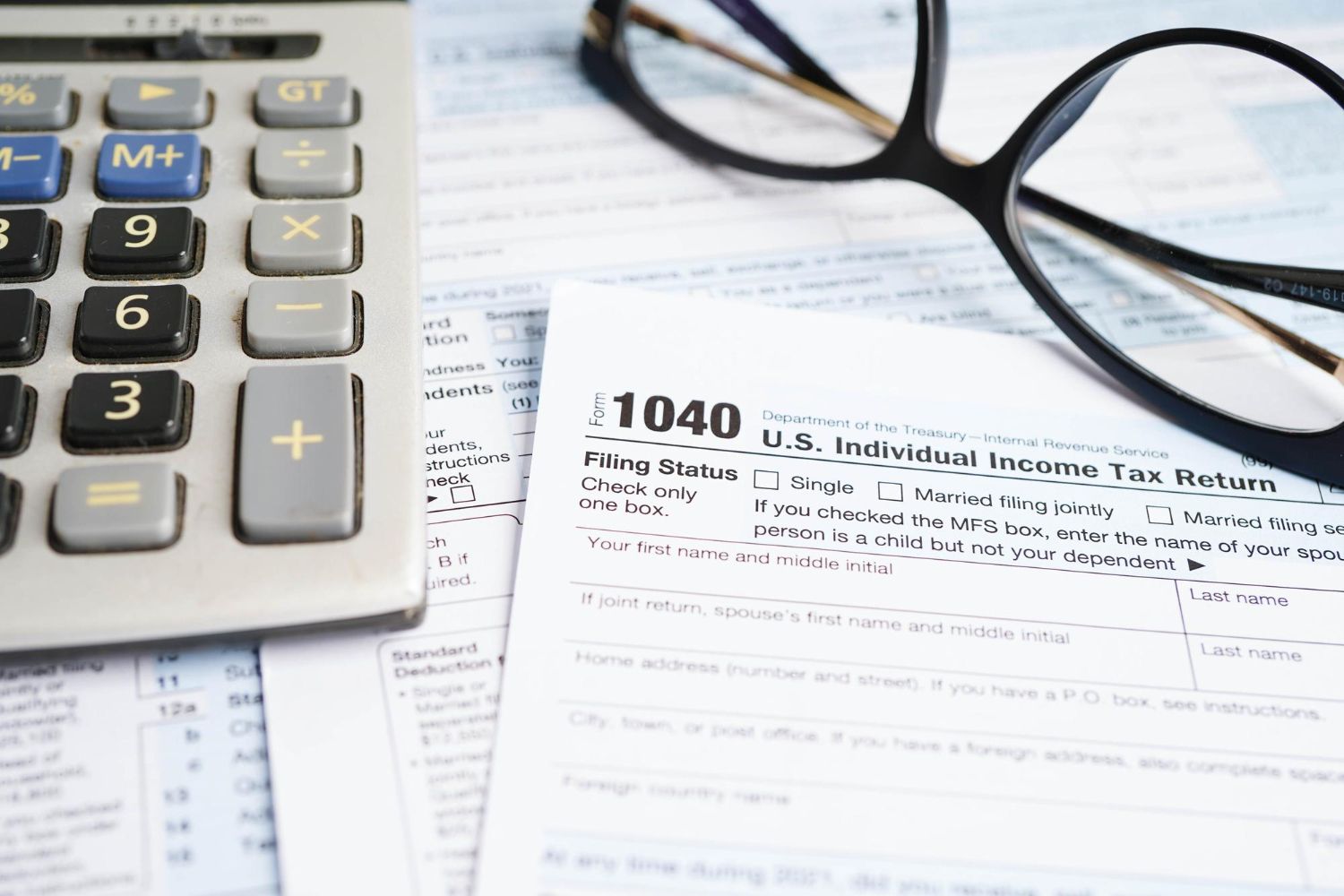Calculator, glasses, and 1040 tax form on a desk.