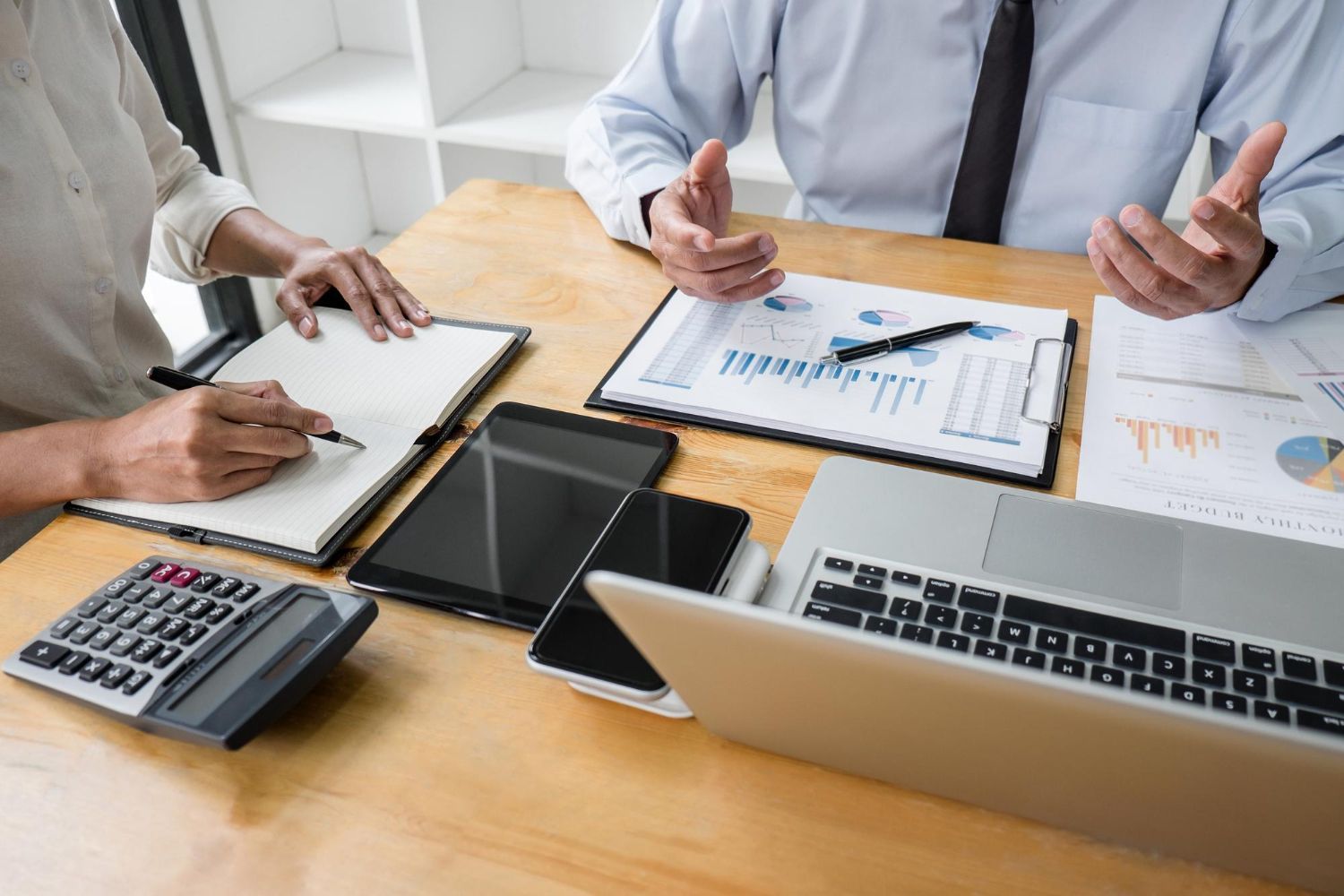 Two people reviewing documents, charts, and a laptop at a table, discussing finances.
