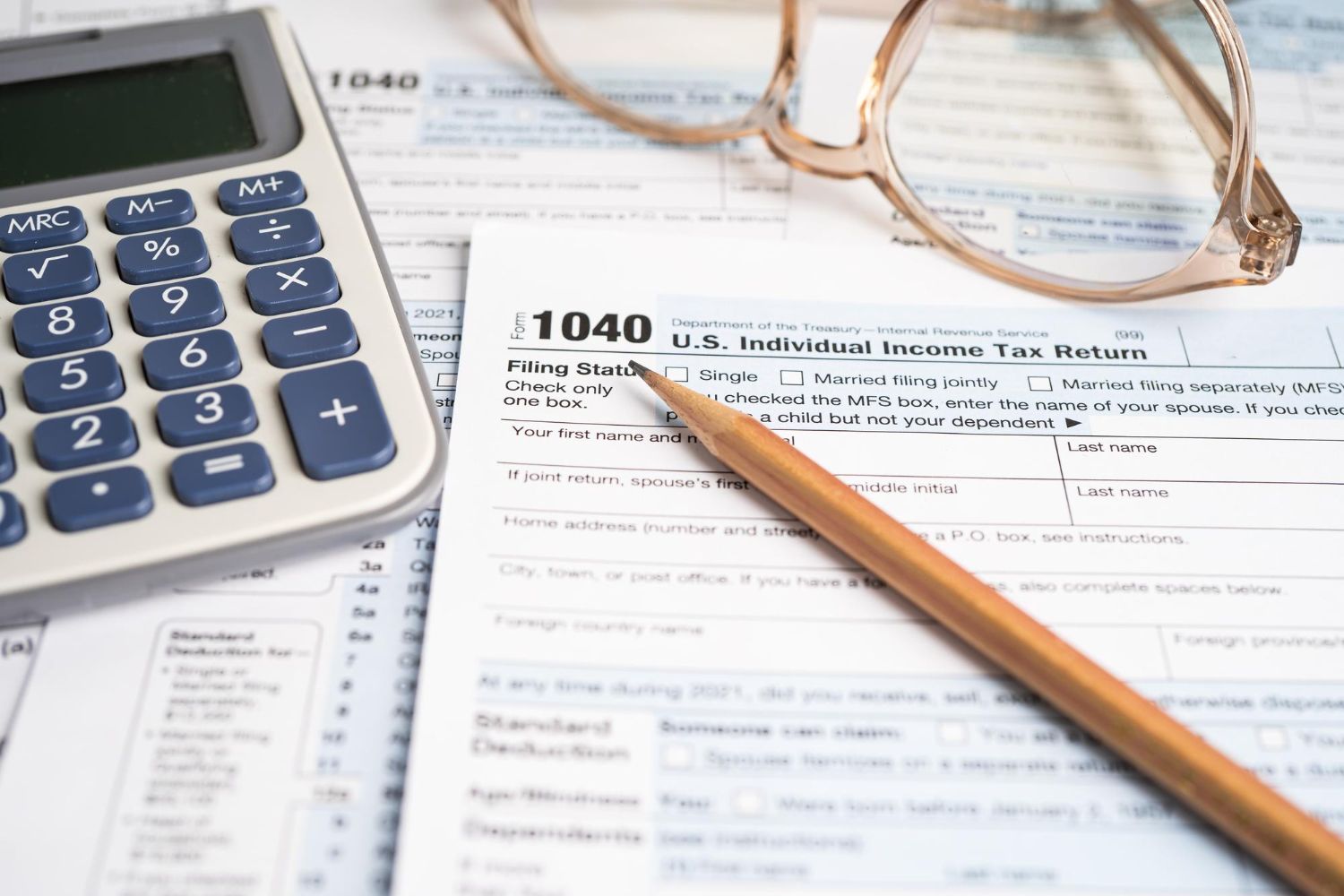 Calculator, glasses, and pencil on top of a U.S. 1040 tax form; preparing for tax return.
