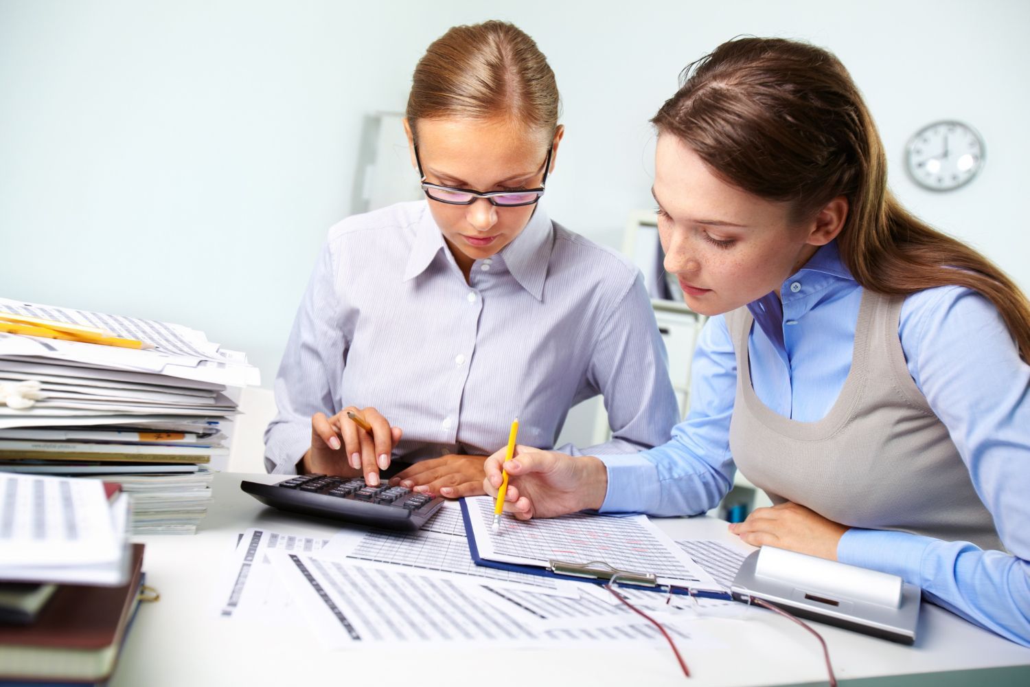 Two people at a desk reviewing documents and using a calculator in an office.