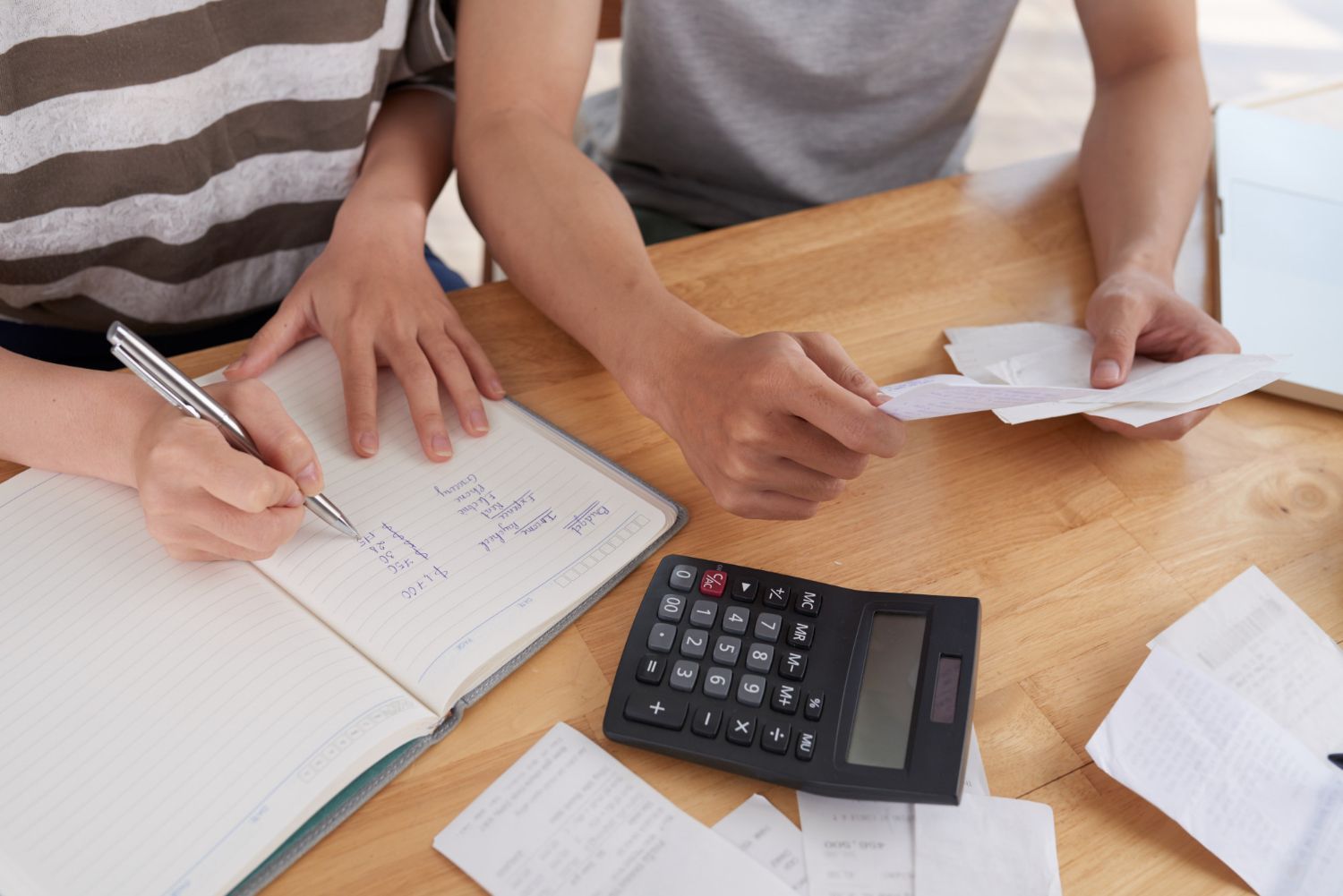 Couple reviews financial documents, making calculations with calculator and pen on a table.