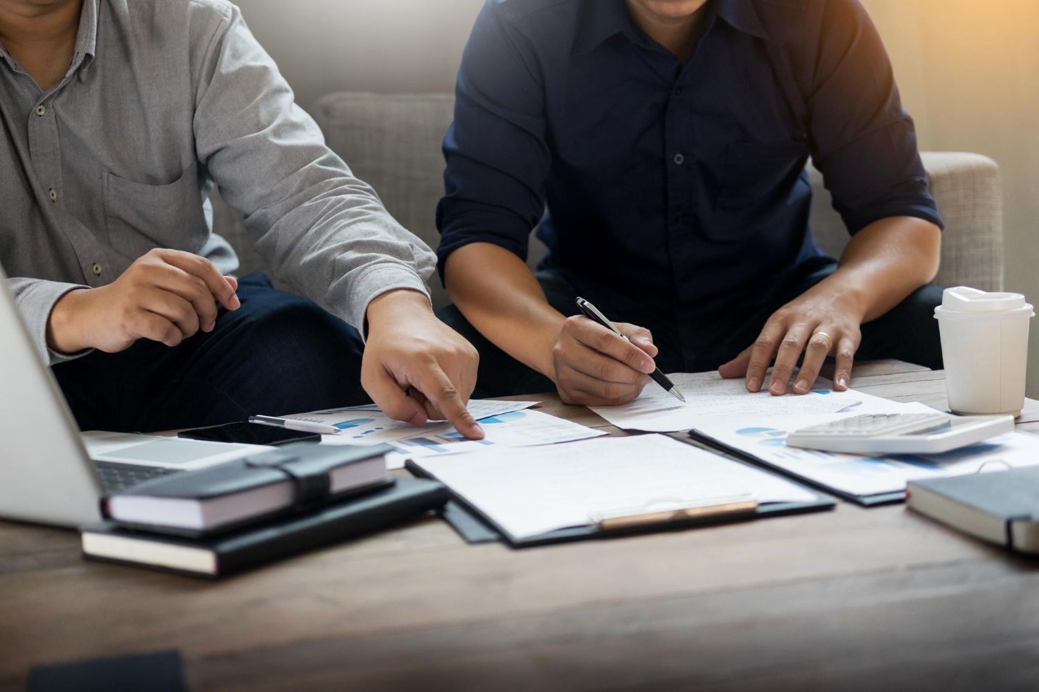 Two men reviewing paperwork, using a laptop, and taking notes on a table.