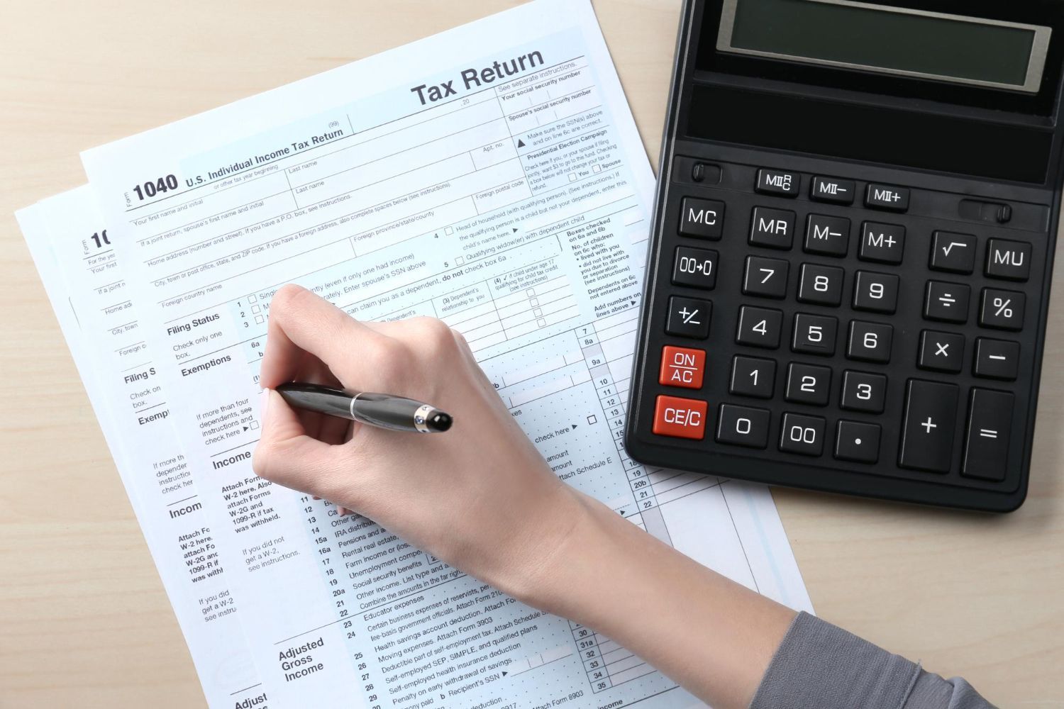 Hand writing on tax form next to a black calculator.