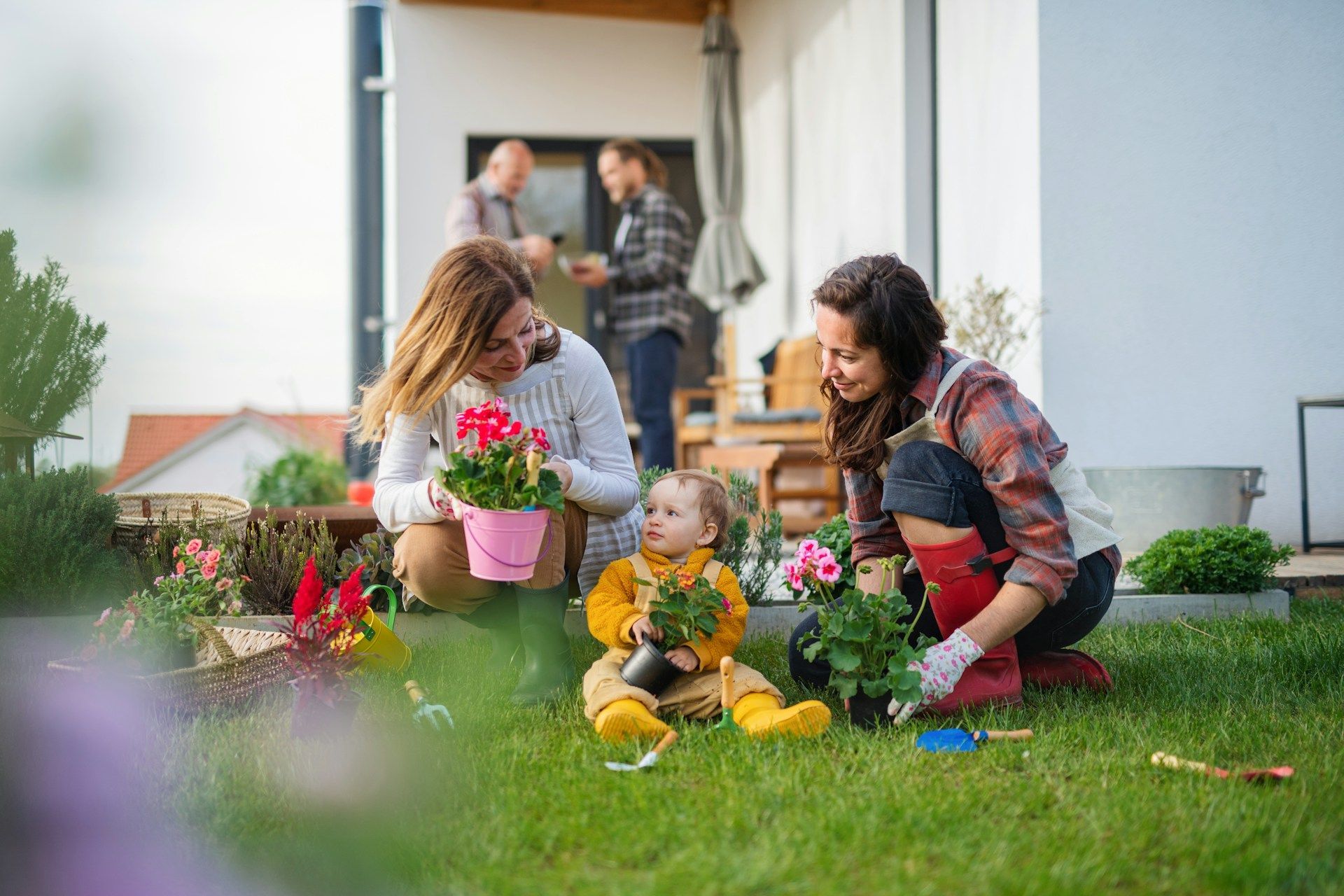 People planting flowers together in a sunny backyard; one is a child.