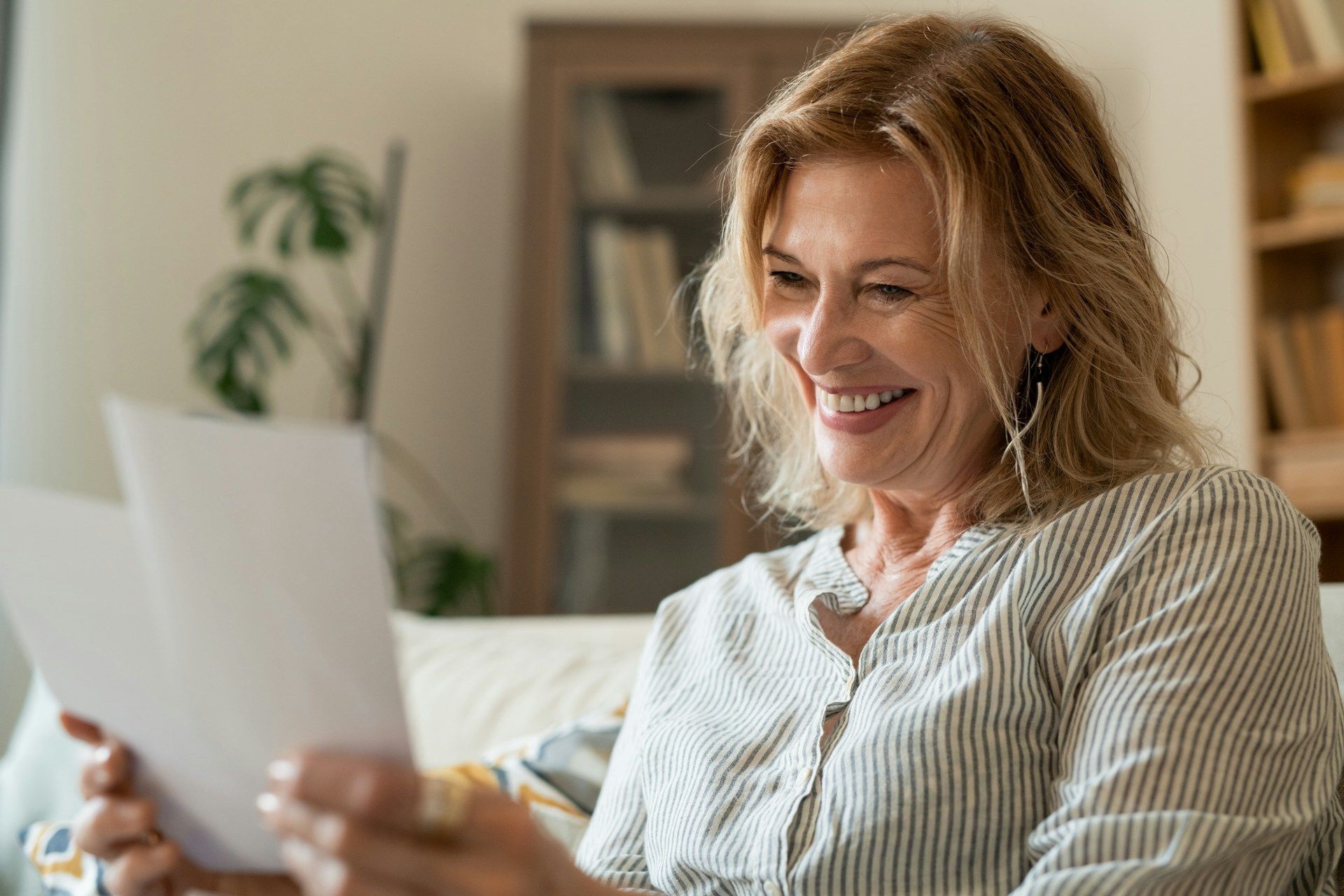 Woman smiling while reading papers in a home setting.