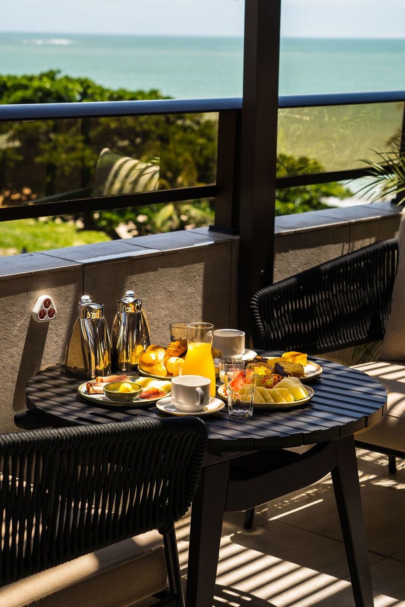 Uma mesa com pratos de comida em uma varanda com vista para o oceano.