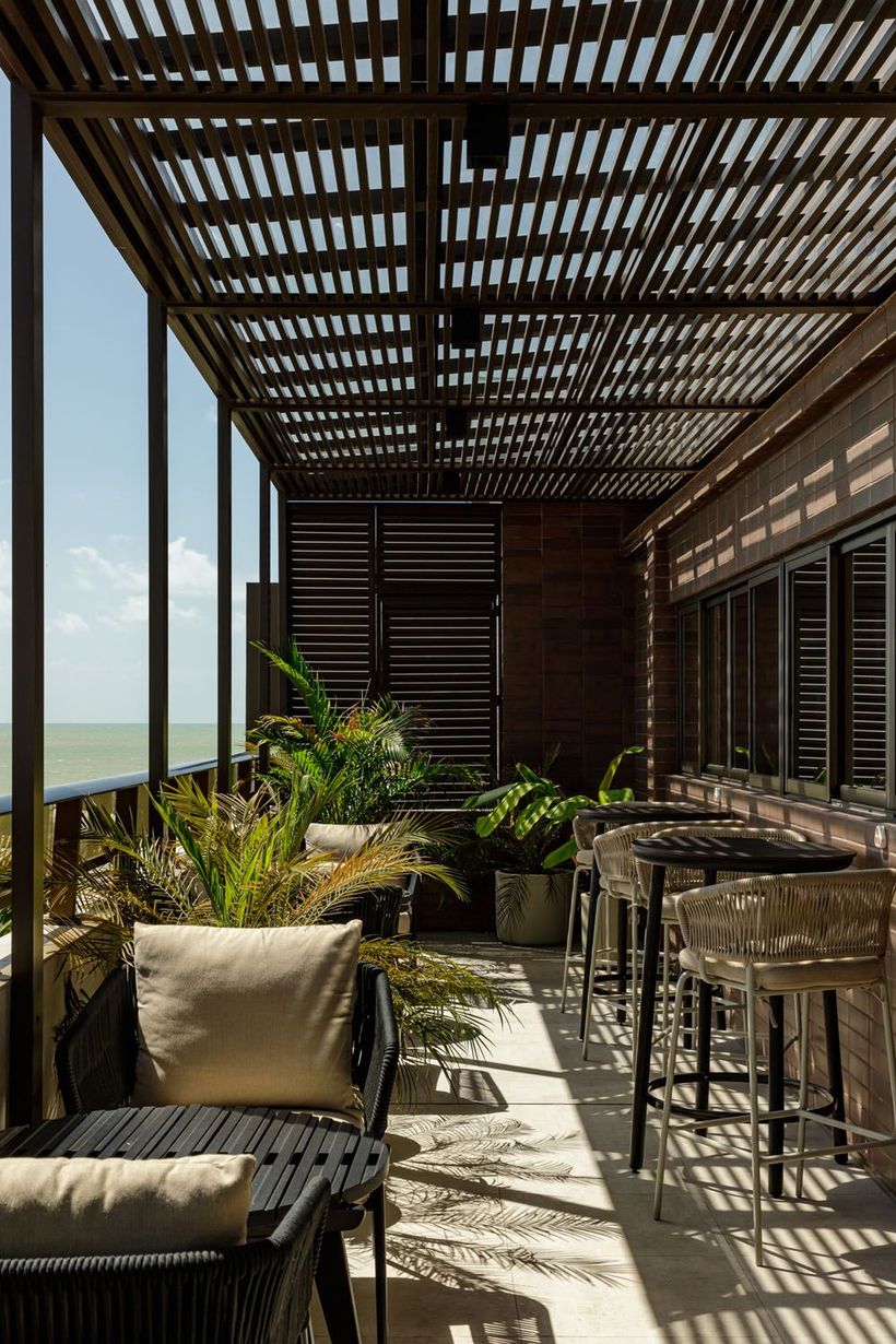 Uma varanda com pérgola, cadeiras, mesas e plantas.